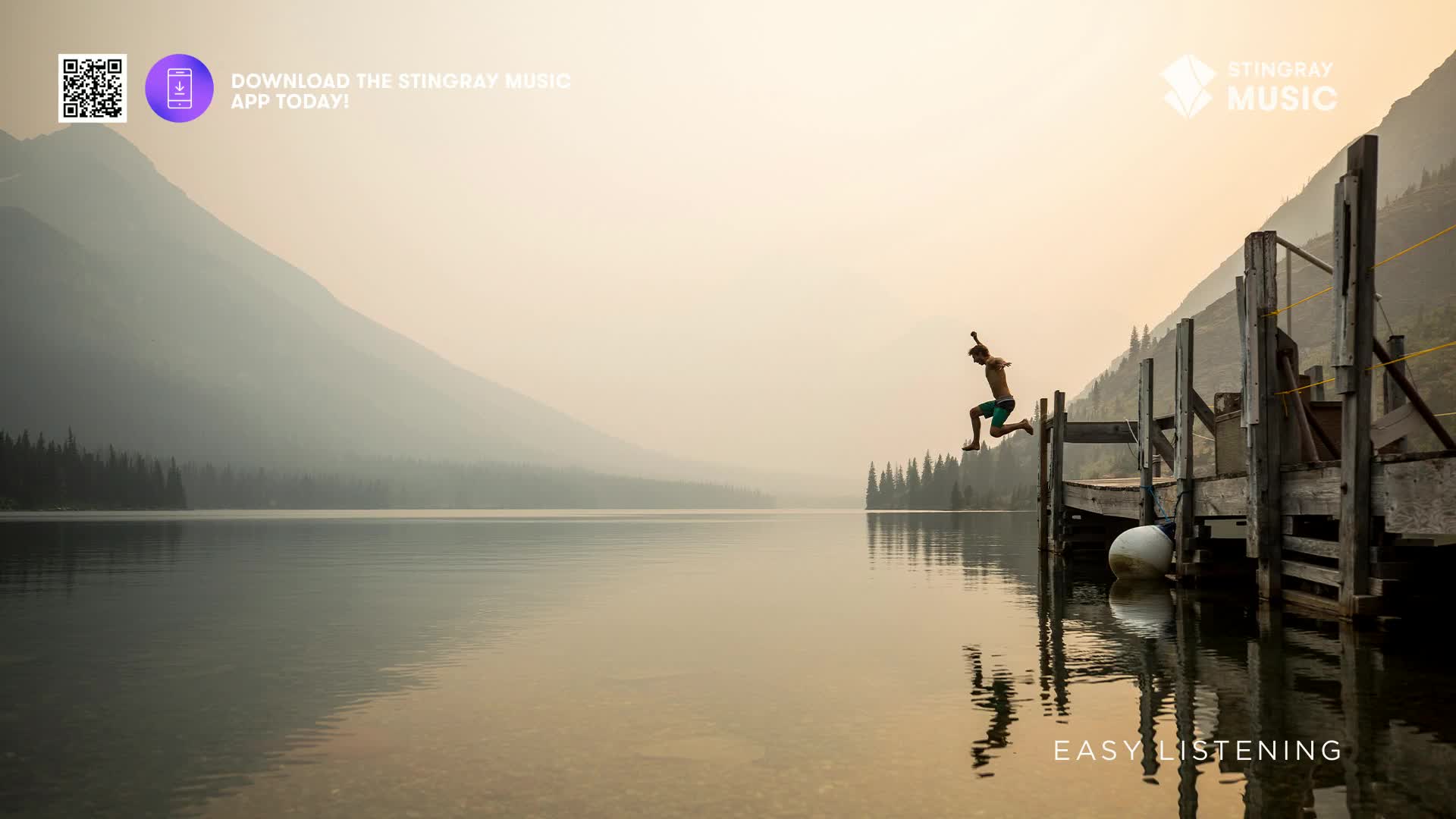 A young person leaps from a wooden dock into a calm lake, silhouetted against a hazy, mountainous backdrop. The water perfectly mirrors the scene, creating a serene Canadian summer moment. A young person leaps from a wooden dock into a calm lake, silhouetted against a hazy, mountainous backdrop. The water perfectly mirrors the scene, creating a serene Canadian summer moment.