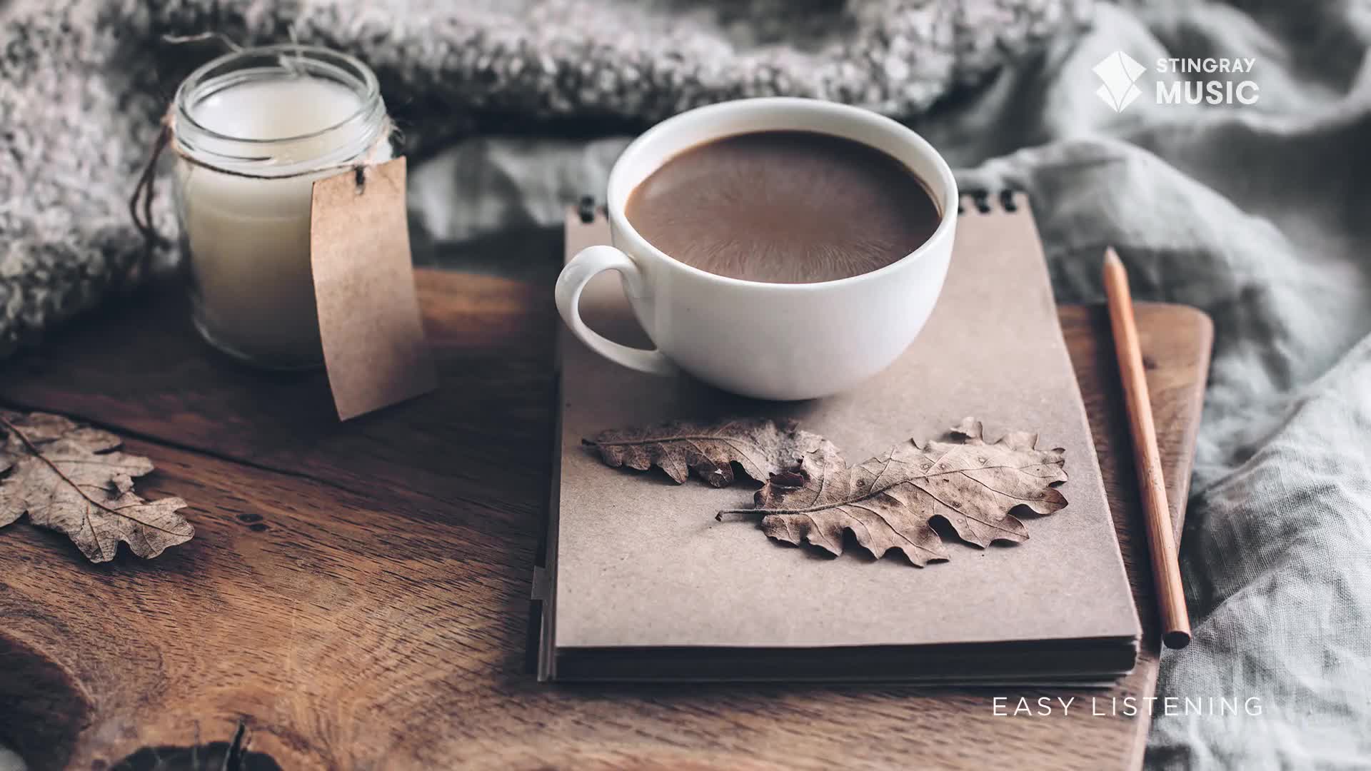 A mug of coffee sits on a notebook, surrounded by dried leaves. A candle in a jar rests nearby, its label a simple brown tag. A mug of coffee sits on a notebook, surrounded by dried leaves. A candle in a jar rests nearby, its label a simple brown tag.