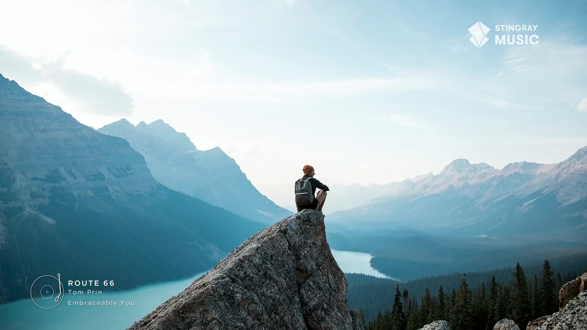 A lone figure sits on a rocky precipice, gazing out at the vast Canadian Rockies. The Stingray Music logo and "Route 66" by Tom Prin, "Embraceable You" are subtly placed, hinting at the soundtrack to this serene moment.