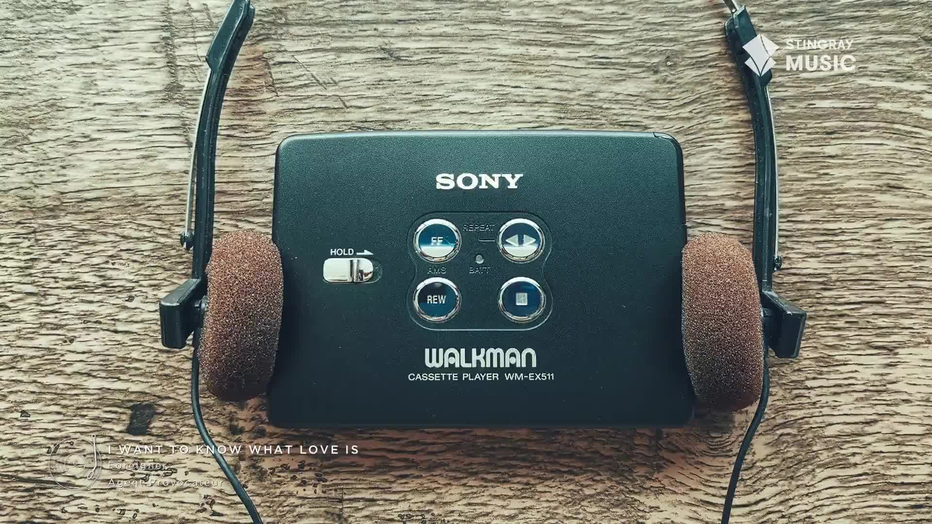 A black Sony Walkman sits centered on a wooden surface, its buttons and the "WALKMAN" logo clearly visible. The headphones, with their brown foam ear pads, are draped on either side, ready to deliver some Stingray Everything '80s from Canada.
