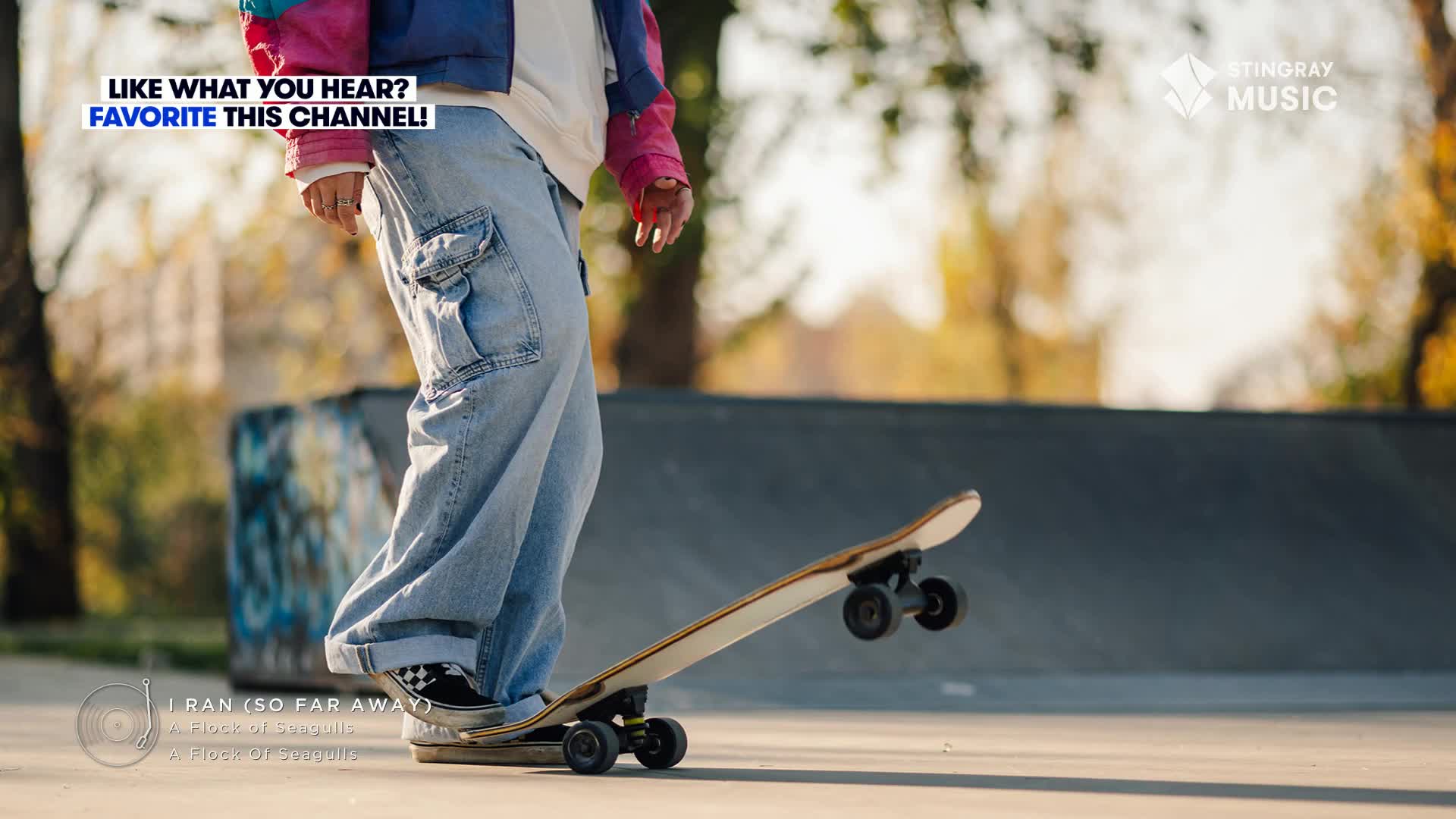 A skateboarder, clad in '80s-style clothing, is lifting the front wheels of their board. The wheels spin in the air as they prepare to launch.
