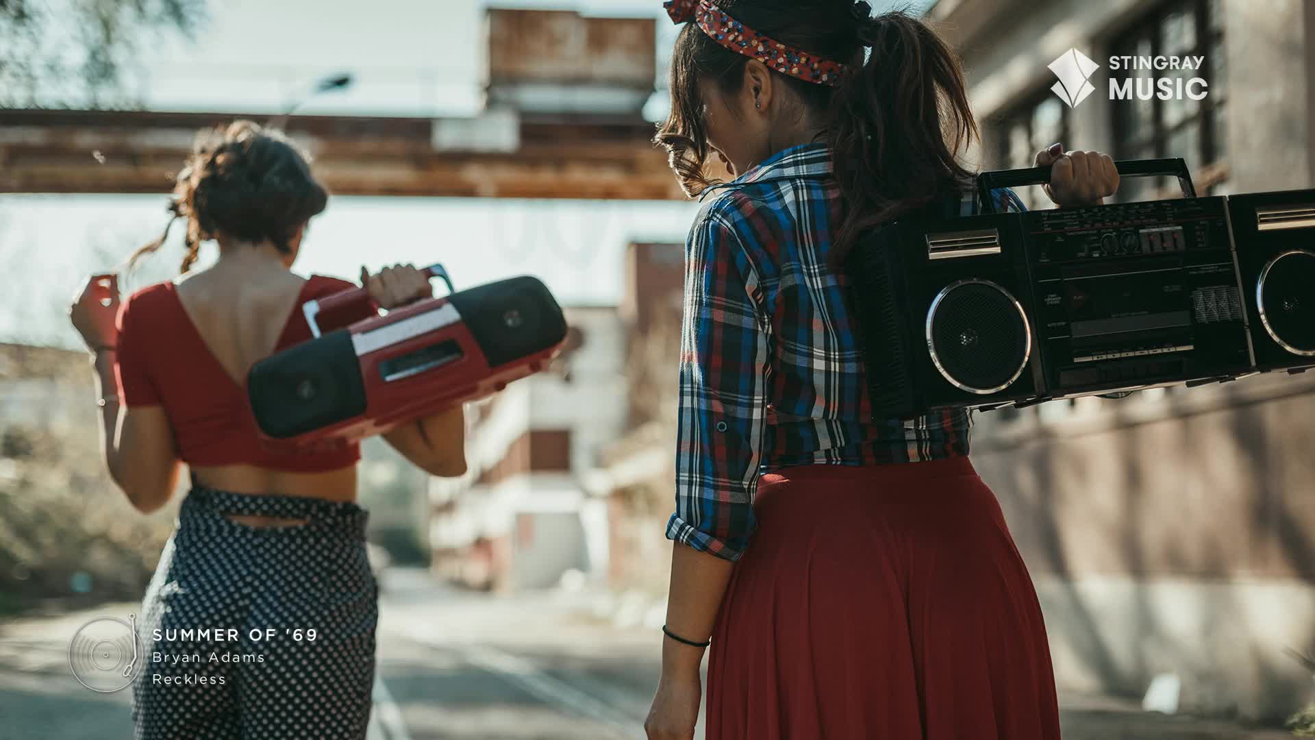Two women stride down a sunlit street, each carrying a boombox on their shoulders. The red and black radios, a perfect soundtrack for a Canada-themed Stingray Everything '80s moment, are ready to blast.
