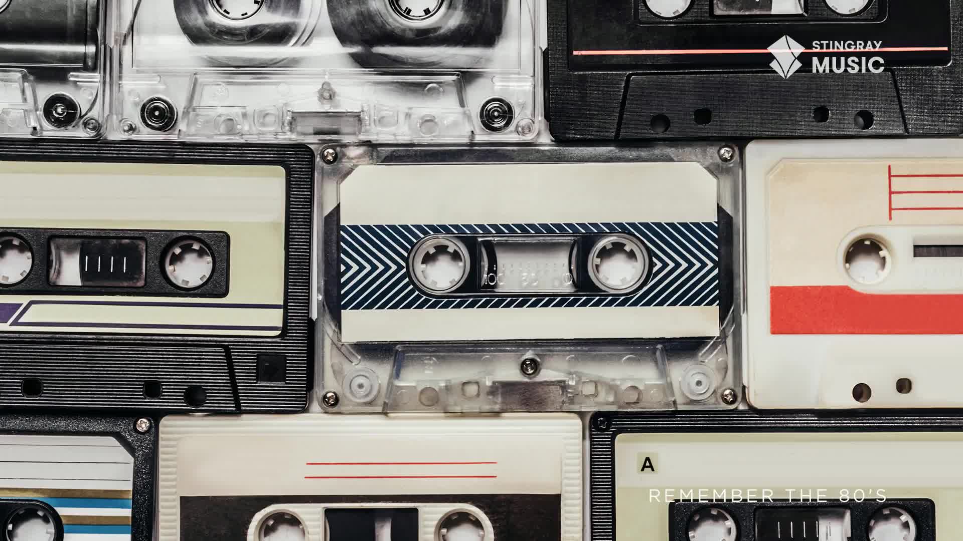 Cassette tapes, a nostalgic reminder of the 80s, are arranged in a grid. The clear plastic cases and labels with their bold colors and designs are all on display.
