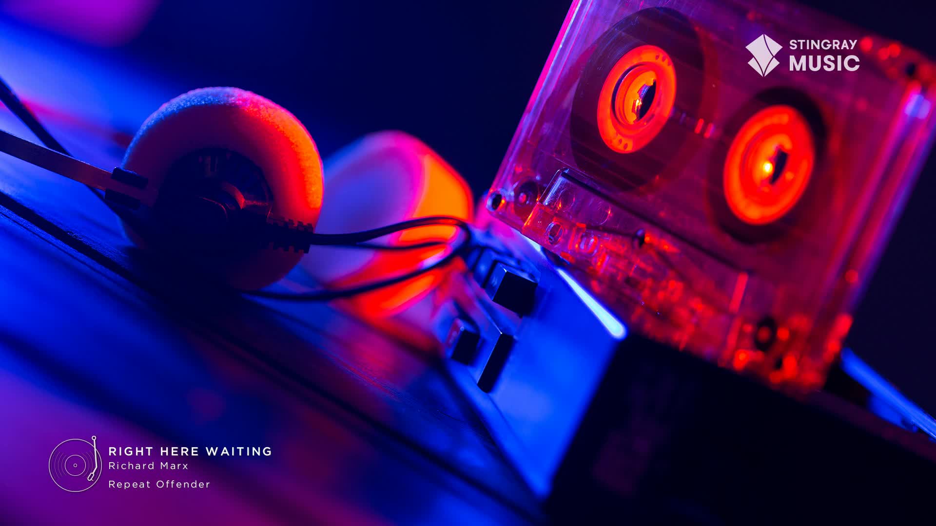 Headphones with orange earcups sit next to a clear cassette tape, both bathed in a mix of blue and red light. The tape's spools glow, and the whole scene feels like a flashback to Stingray Everything '80s.
