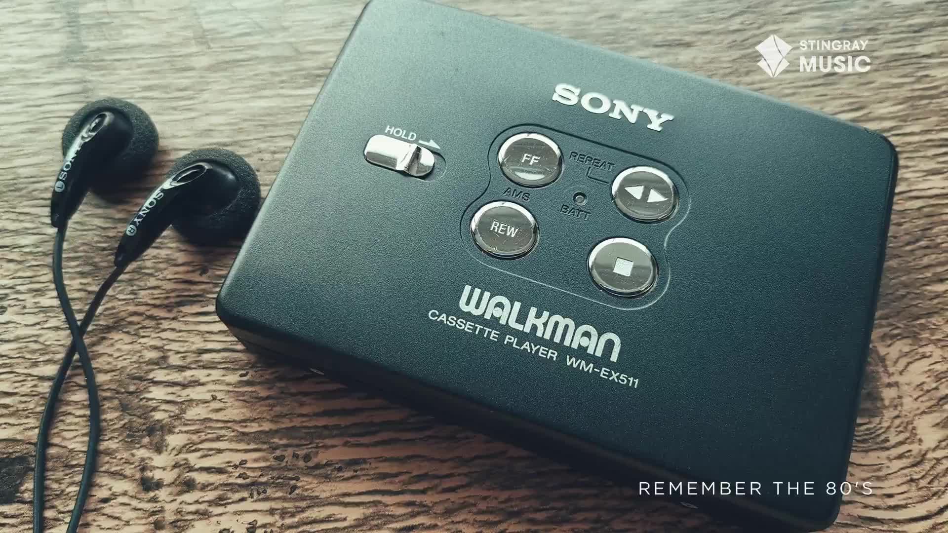 A black Sony Walkman cassette player sits on a wooden surface, its buttons and the "WALKMAN" label clearly visible.  Black earbuds with foam covers are laid out beside it, ready for a dose of Stingray Everything '80s.
