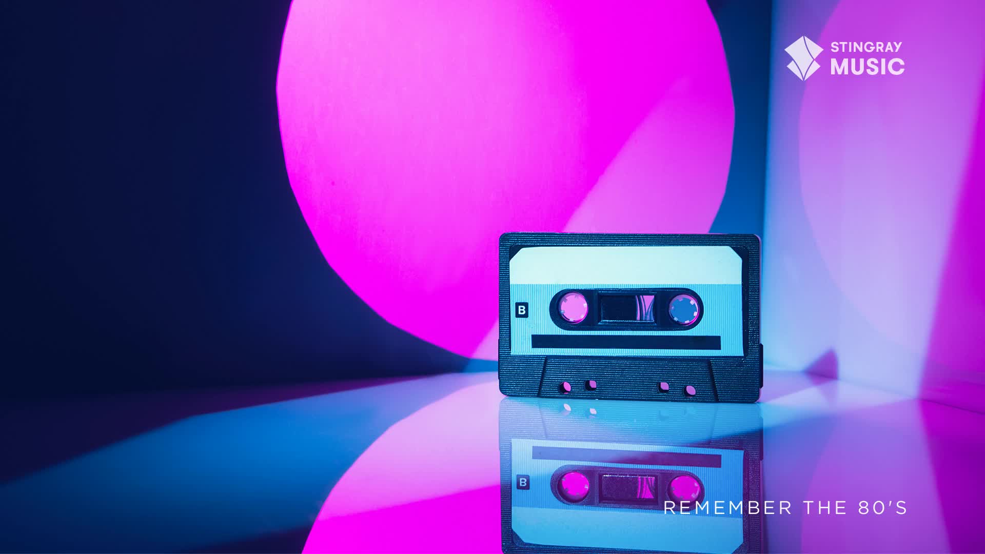 A retro cassette tape sits on a reflective surface, illuminated by vibrant pink and blue light. The Stingray Music logo and the words "Remember the 80's" are visible, evoking a nostalgic vibe.

