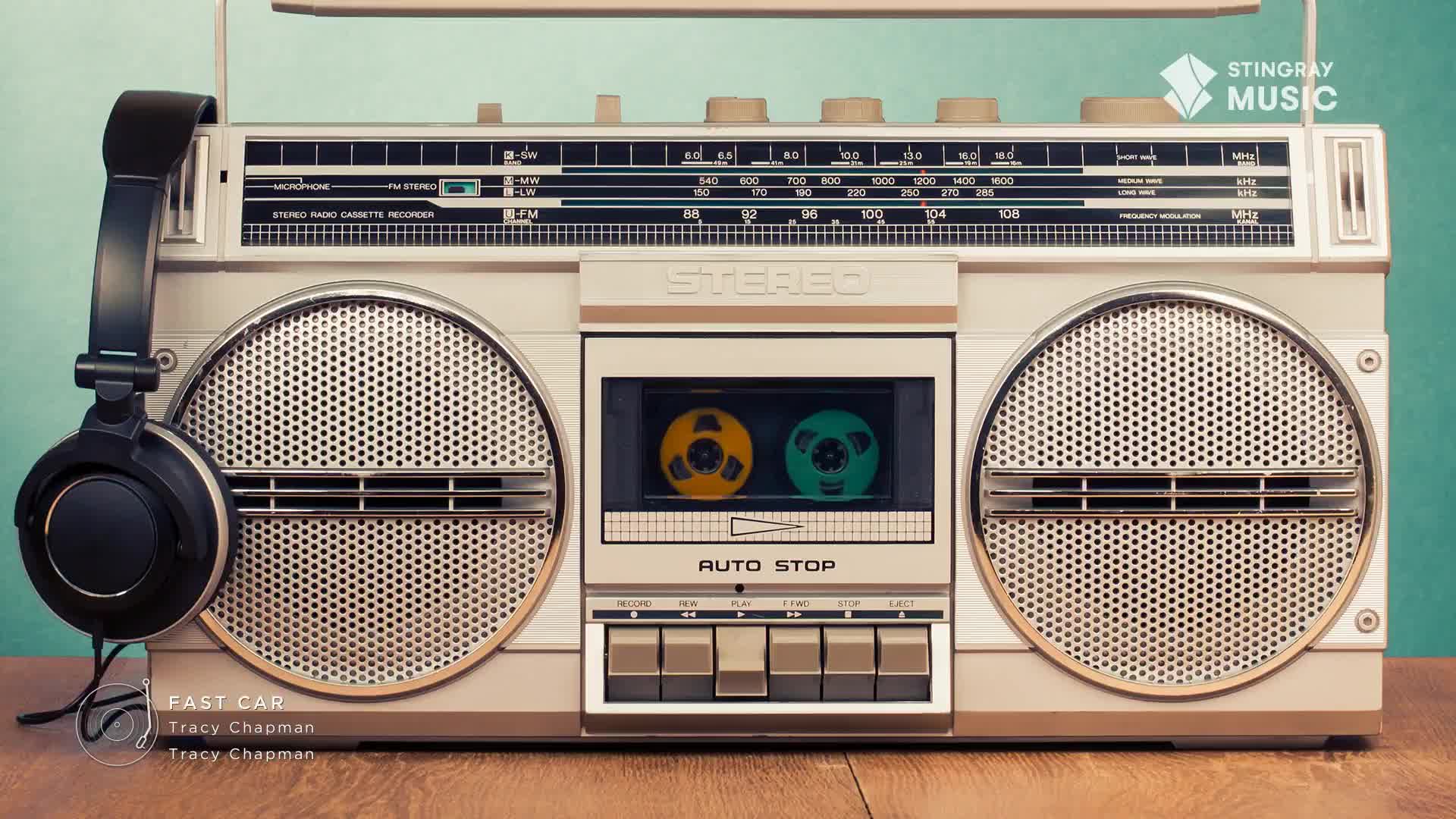 A vintage boombox sits on a wooden surface, with black headphones resting on its side. The cassette player's window reveals two colorful tapes, ready for a Stingray Everything '80s playlist.
