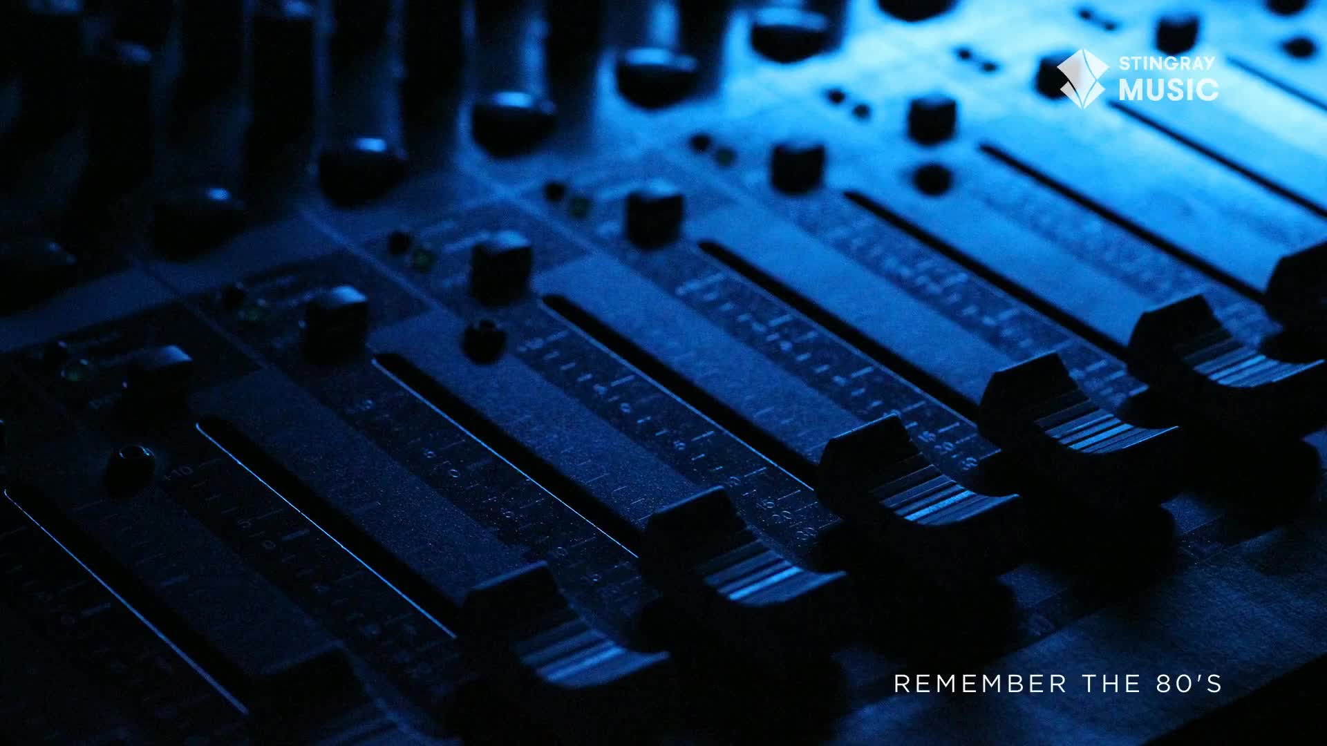 A soundboard, bathed in cool blue light, fills the frame. The faders, ready to be adjusted, are lined up in a row, a reminder of Stingray Everything '80s.
