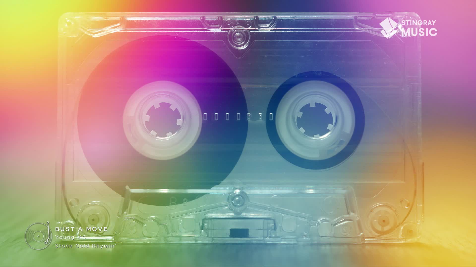 A clear cassette tape, like the ones from Stingray Everything '80s in Canada, sits against a vibrant, rainbow-colored backdrop. The tape's spools are visible, and the "Bust a Move" song title is in the corner.
