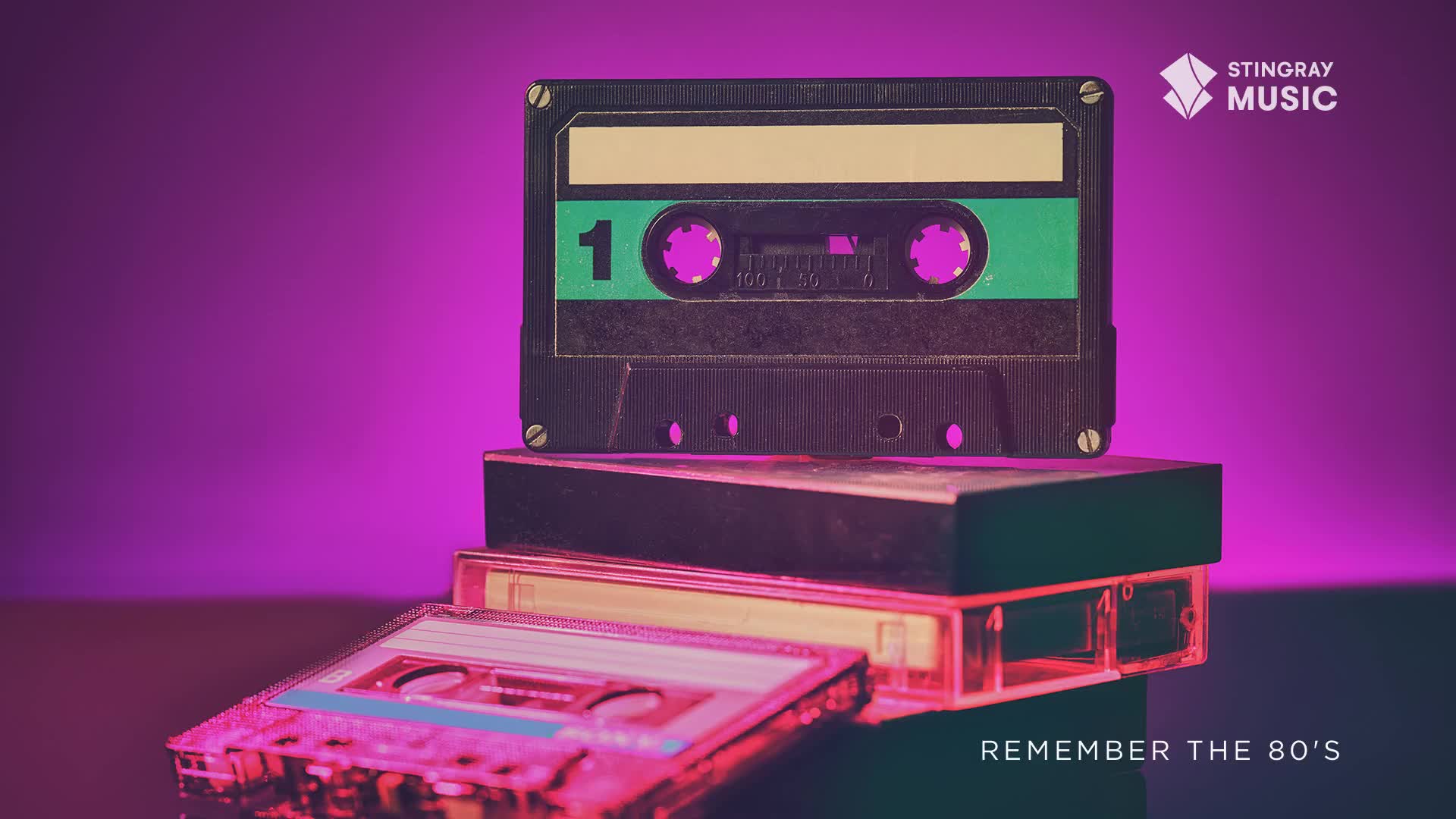 A stack of vintage cassette tapes sits under a vibrant purple light. The top tape, a classic black and green, has a prominent "1" on its label.
