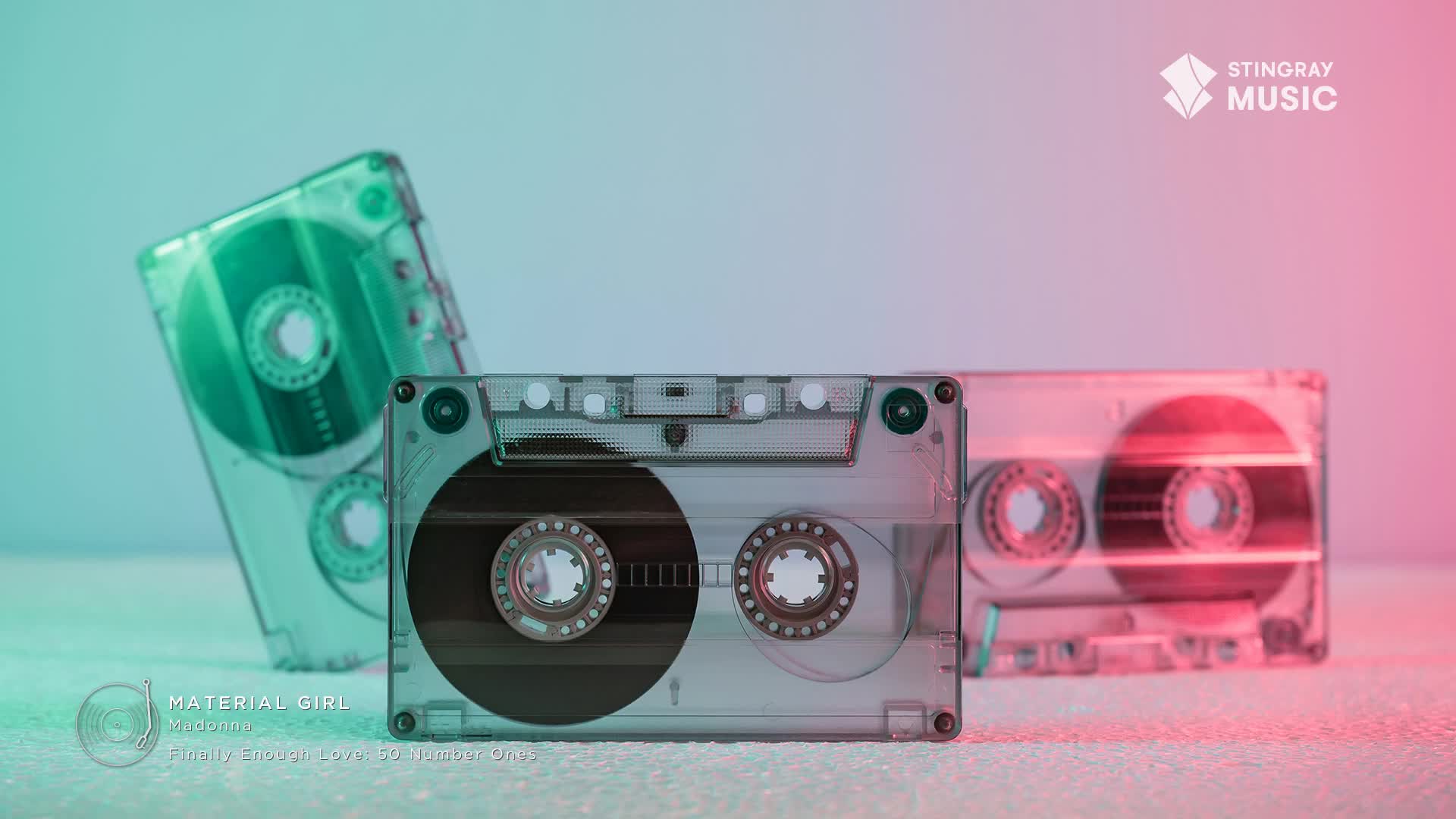 Three clear cassette tapes sit on a surface, bathed in teal and pink light. One tape, tilted on its side, shows its dark magnetic tape spooling.
