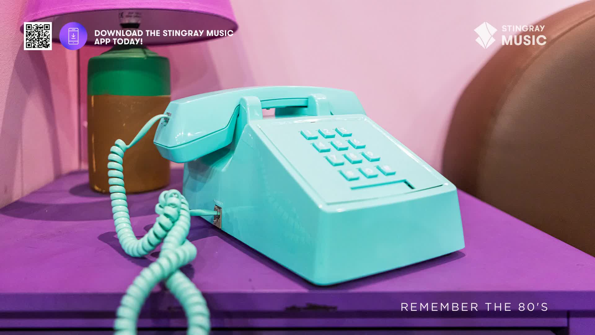 A bright teal rotary phone sits on a purple surface, its coiled cord resting loosely. This is a scene straight out of the 80s, a time when music was king.