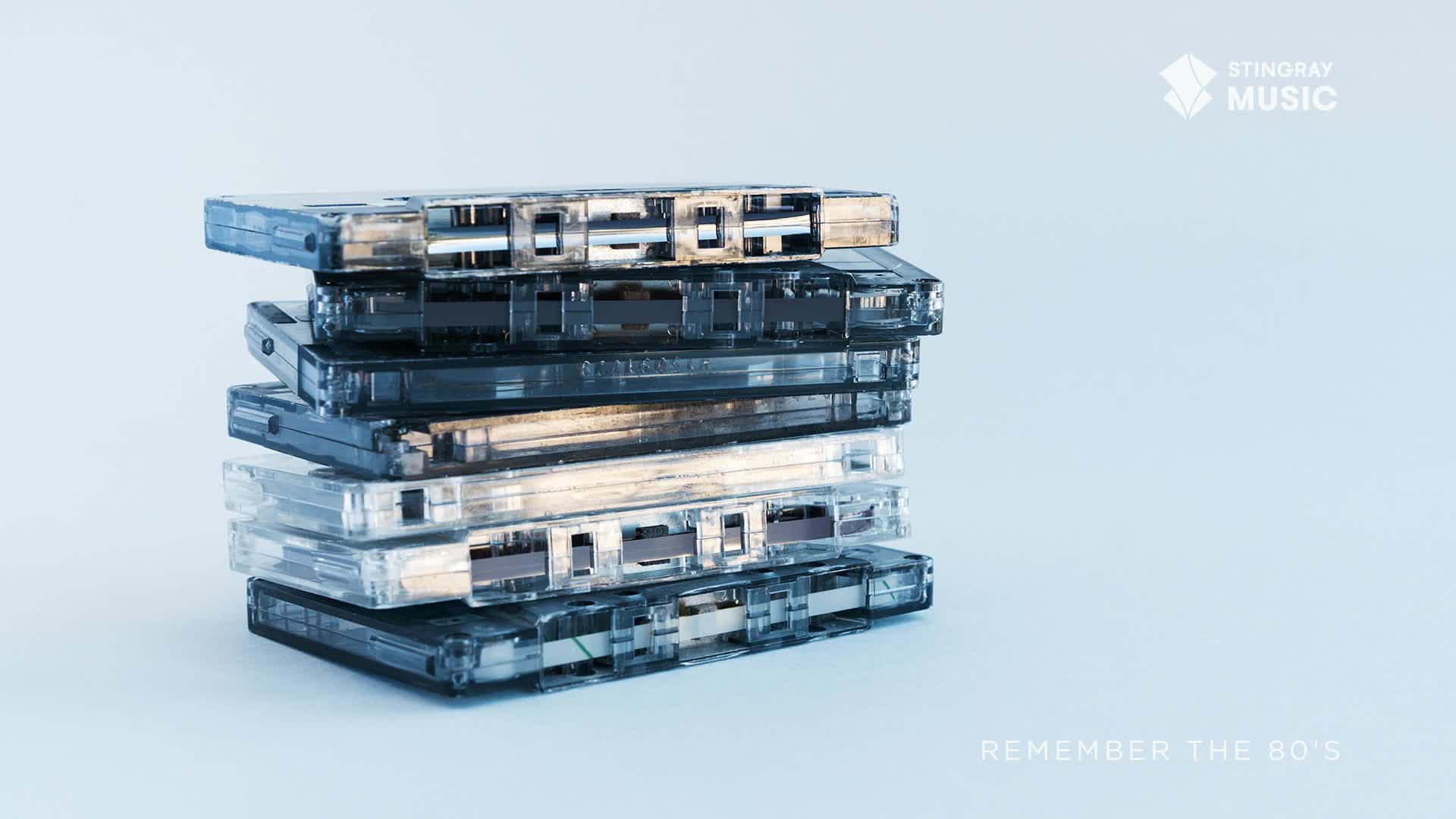 A stack of cassette tapes, some clear and some dark, sits on a pale blue surface. The Stingray Music logo is visible in the upper right corner, hinting at a Canadian connection to this collection of '80s nostalgia.