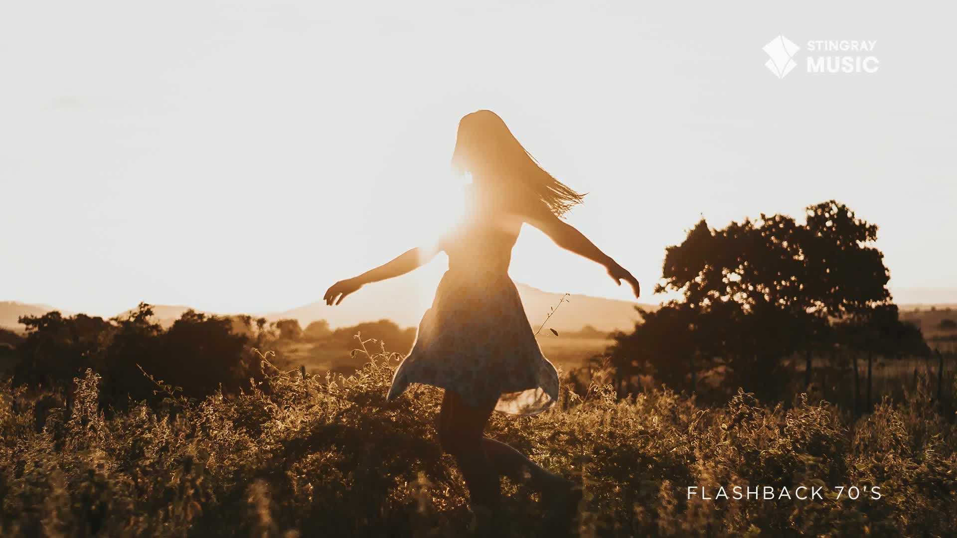 A woman, backlit by the sun, twirls in a field of tall grass. Her dress billows as she spins, her hair streaming out behind her.
