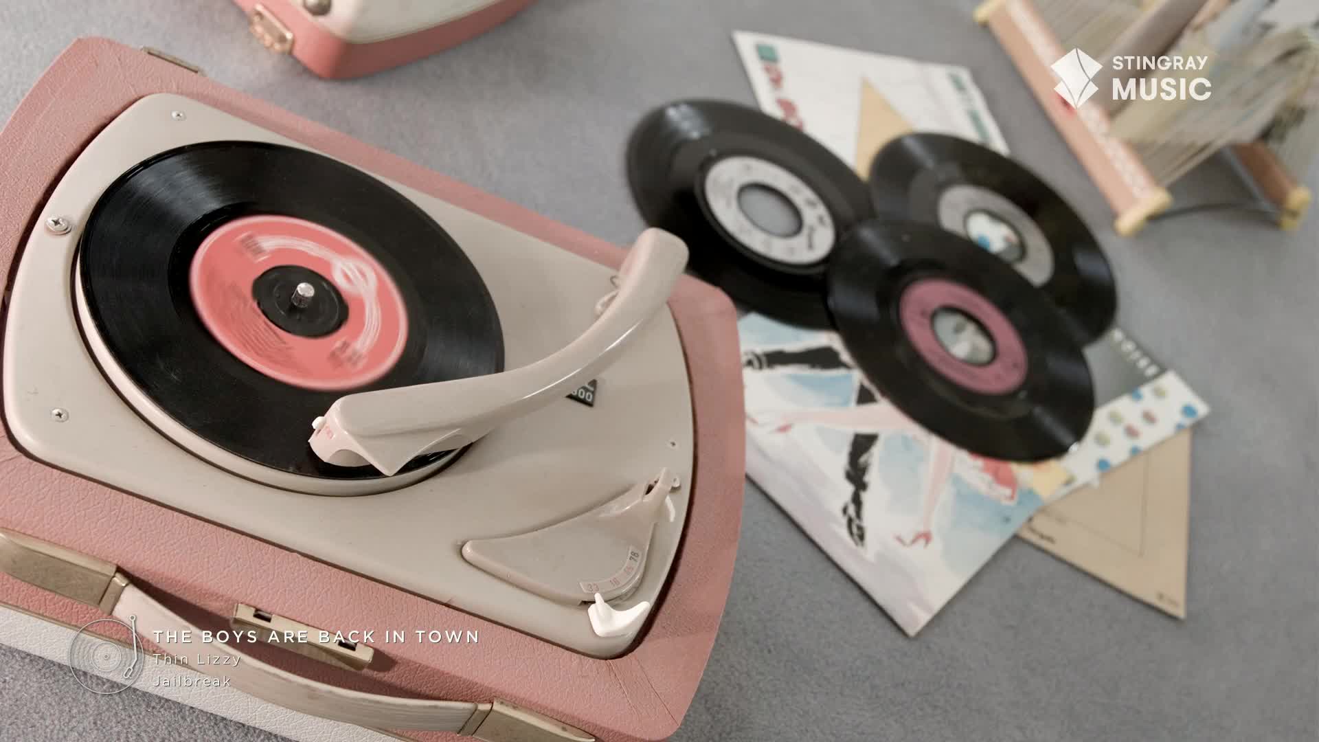 A pink and cream record player spins a 45, the needle tracing its grooves. Several other records and their sleeves sit nearby, a nostalgic nod to the Stingray Flashback 70's from Canada.
