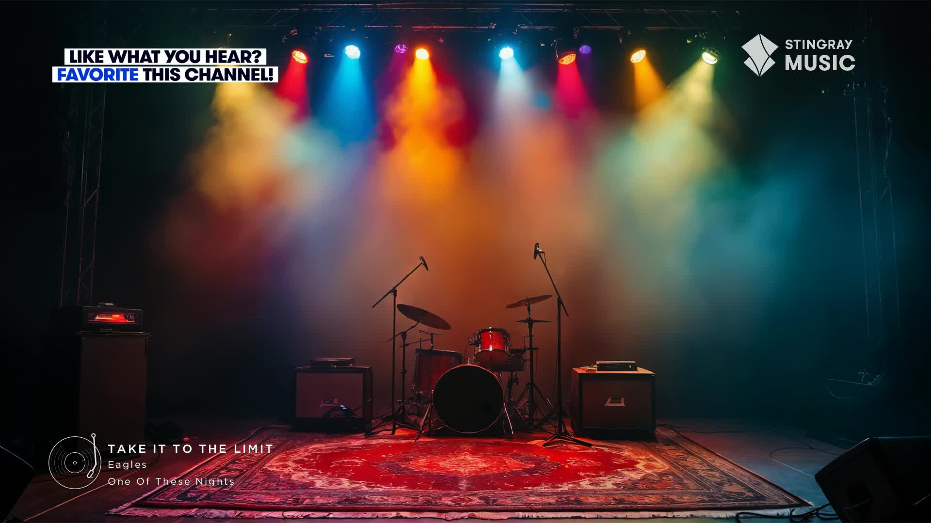 Colored stage lights illuminate a drum set and microphones, casting a warm glow on the vintage rug. The Stingray Flashback 70's is about to begin.
