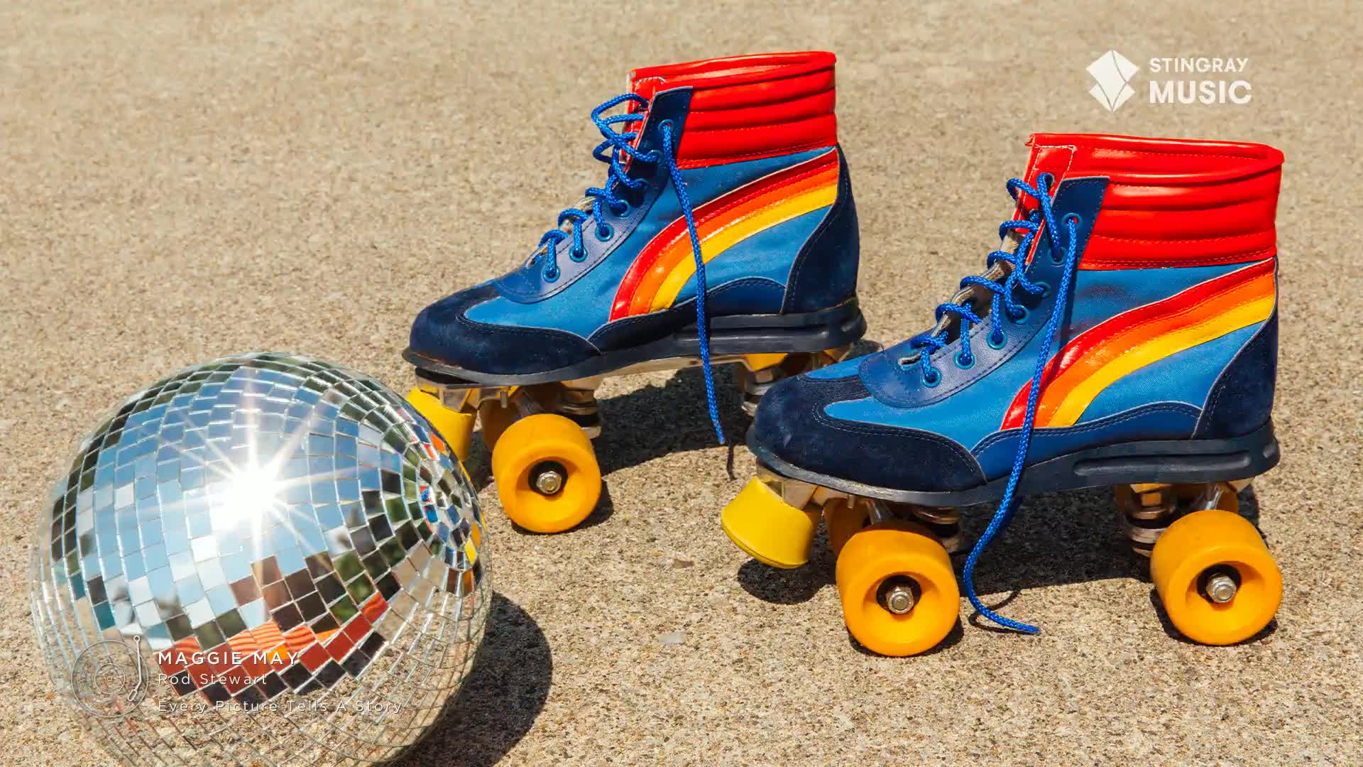 A pair of retro roller skates, blue with a rainbow stripe, sit on a concrete surface next to a disco ball. The skates and the ball likely evoke the Stingray Flashback 70's Canada vibe.
