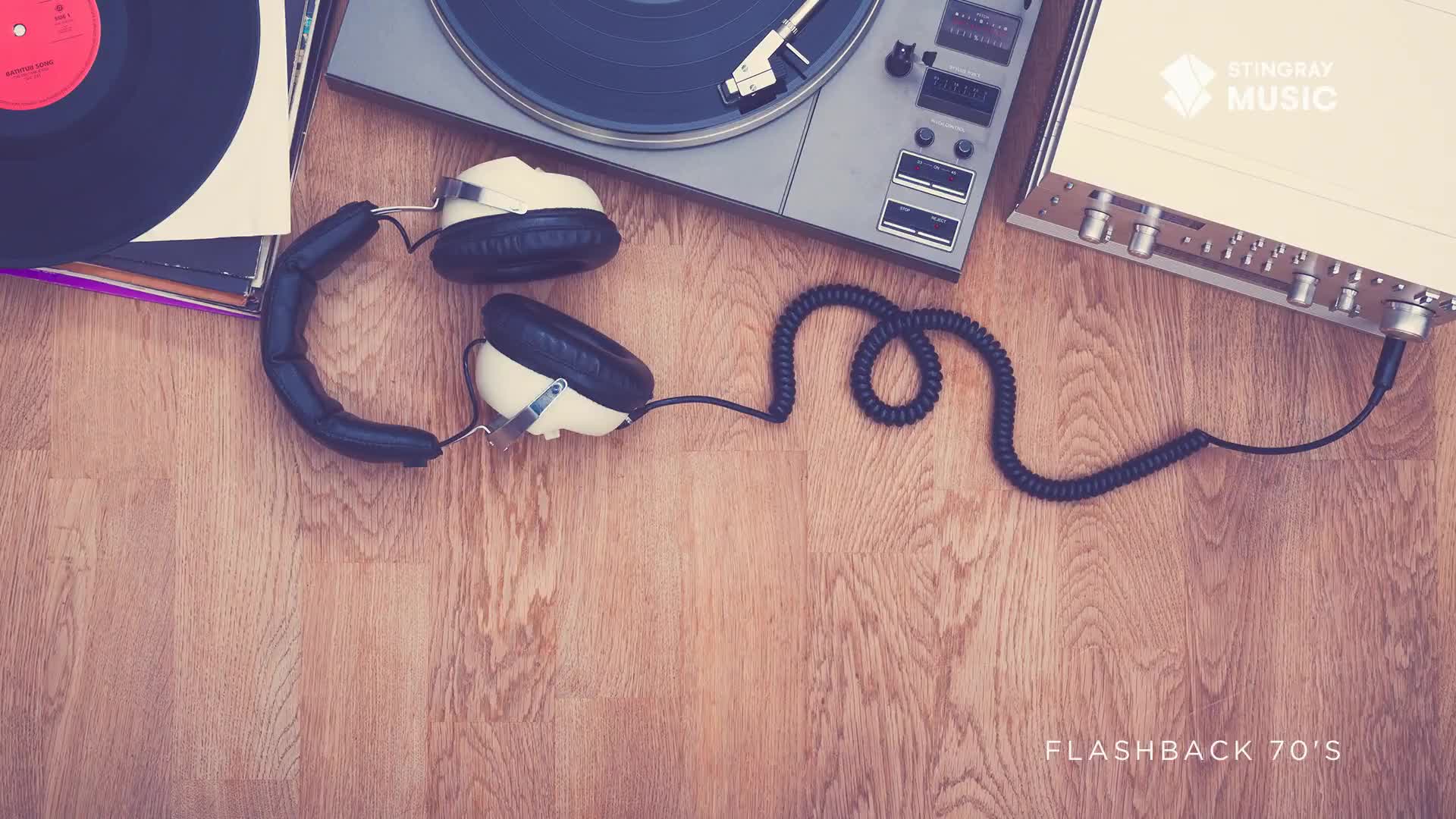 A record spins on a turntable, its needle poised to play. Beside it, a pair of vintage headphones sits, their cord snaking across the wooden floor.
