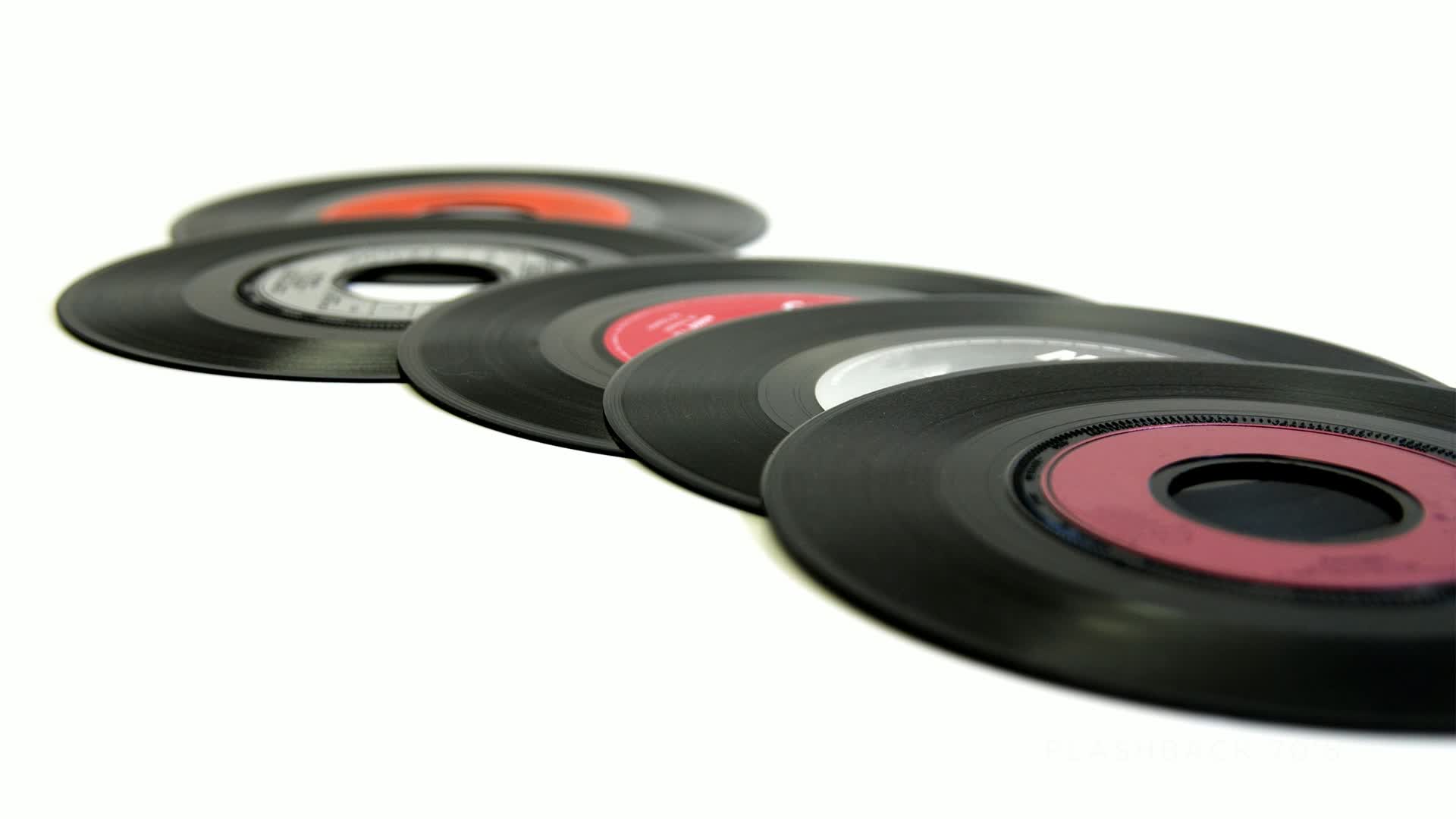 A row of vinyl records, each with a different colored center label, angles across a bright white surface. The black discs, relics of a Stingray Flashback 70's Canada, are slightly overlapping.
