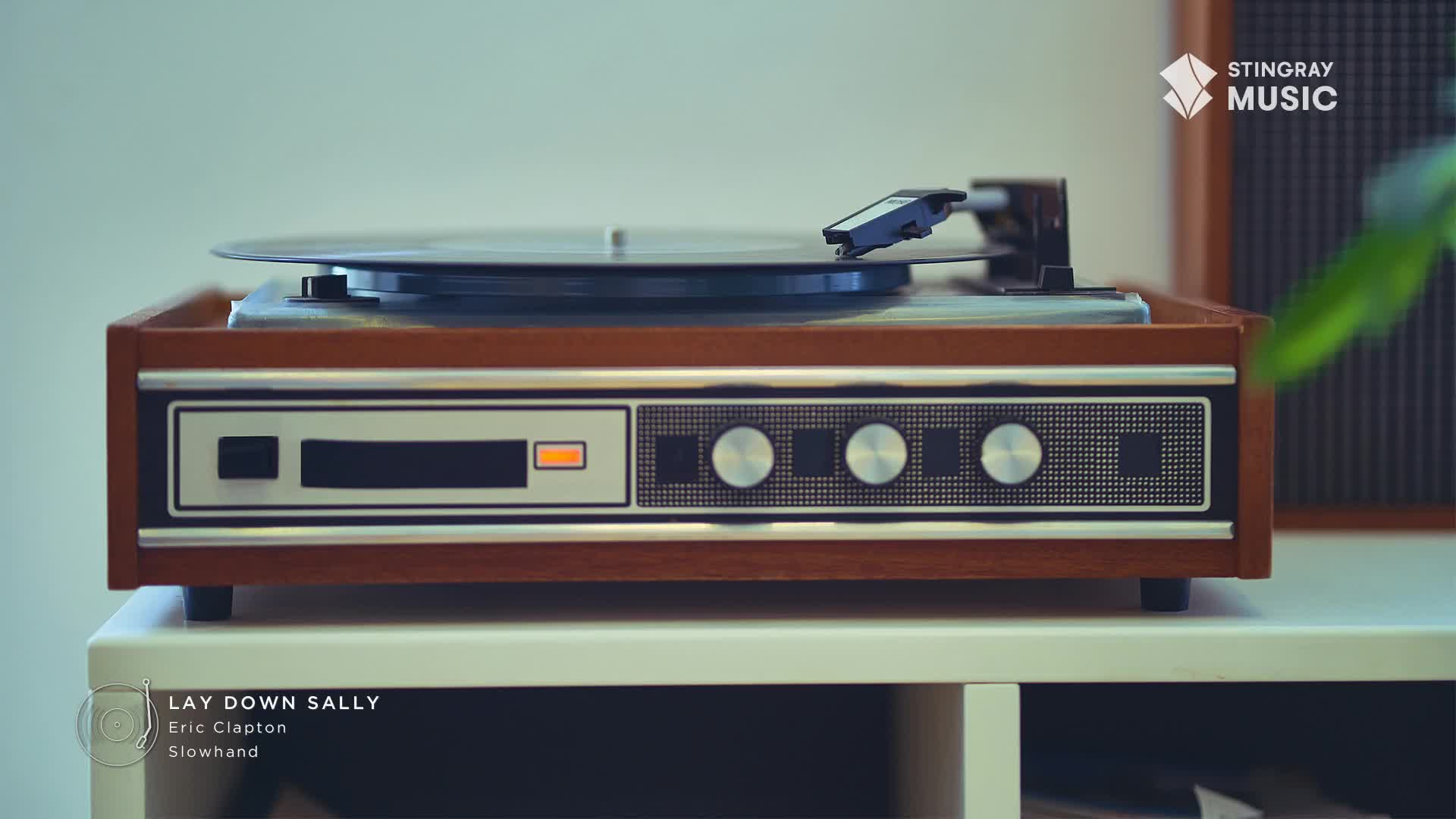 A vintage record player, the kind you'd find in Canada during the Stingray Flashback 70's, is spinning a vinyl record. The needle rests gently on the grooves, ready to play "Lay Down Sally" by Eric Clapton.
