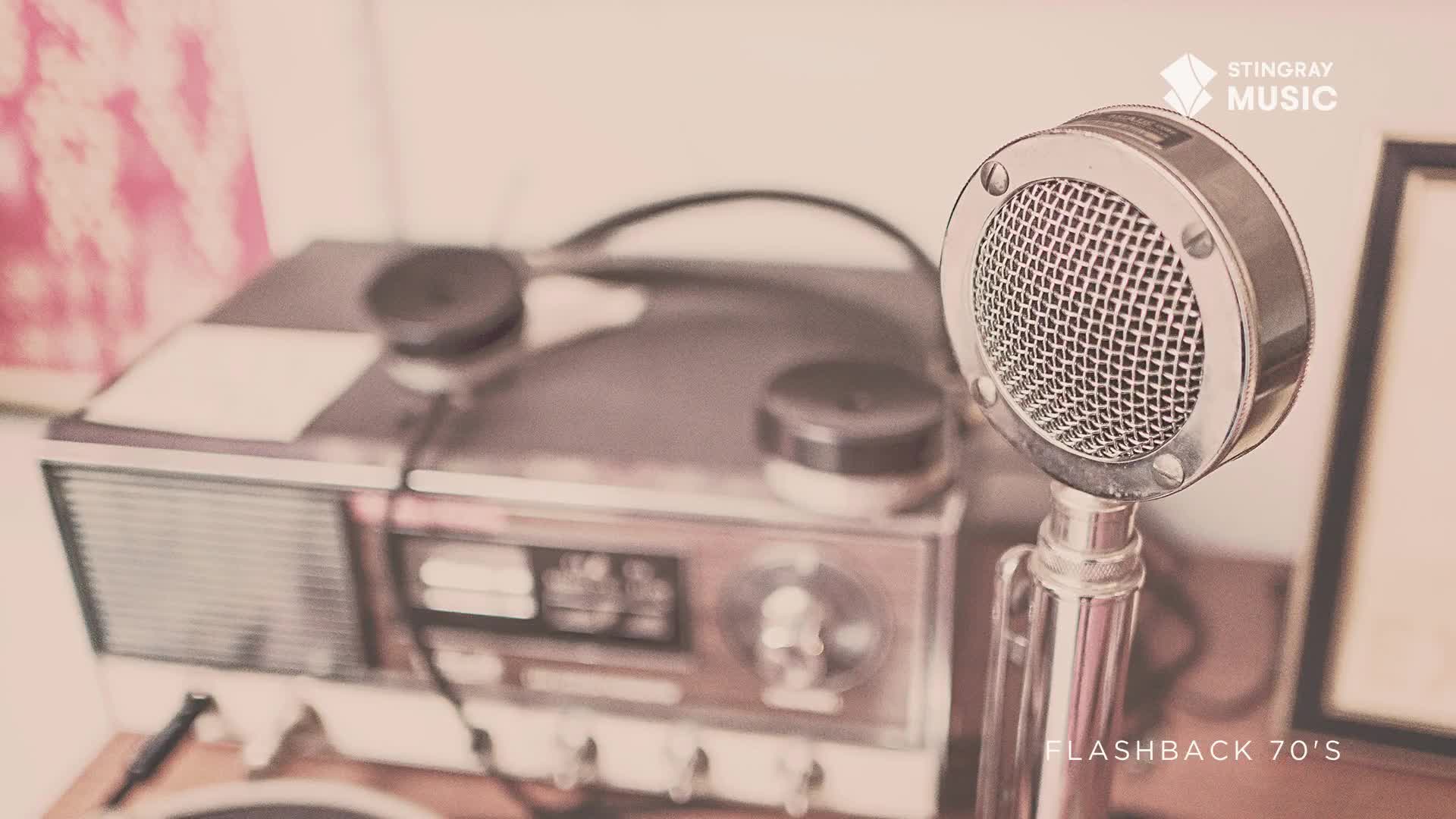 A vintage microphone stands tall, its mesh head reflecting the light. Behind it, a radio sits on a wooden surface, a relic from Canada's Stingray Flashback 70's.
