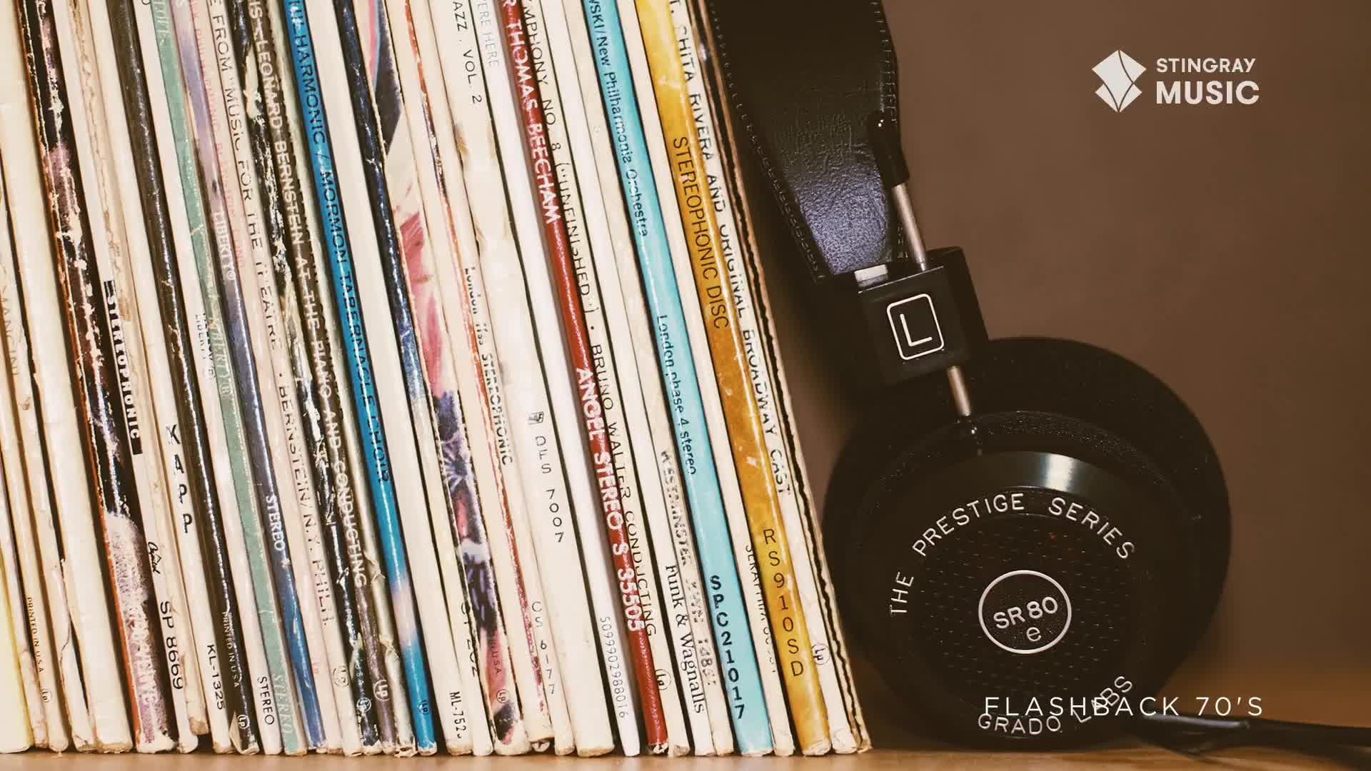 A stack of vinyl records leans against a pair of black headphones, ready for a listen. The "Flashback 70's" logo hints at the music inside, a nostalgic trip from Canada.
