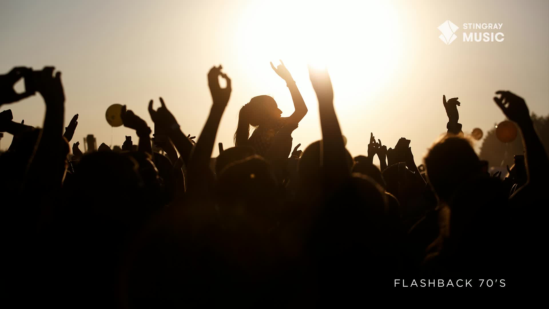 A sea of raised arms and hands reaches toward the sun, silhouetted against the bright sky. A young woman sits atop someone's shoulders, her arms raised in the air, a small figure of pure joy.
