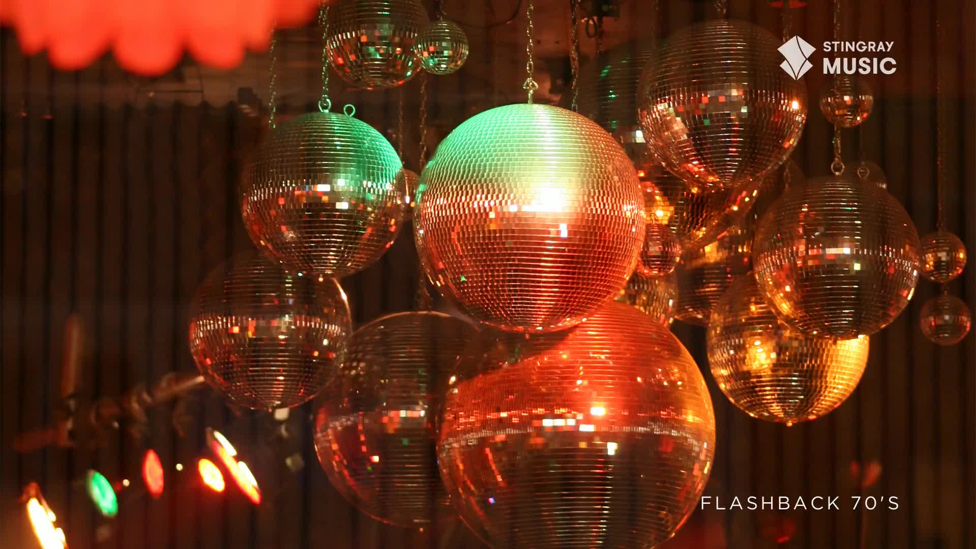 Hanging from the ceiling are several disco balls, each reflecting the warm, orange and green light of the room. It's a scene straight out of a Stingray Flashback 70's party in Canada.
