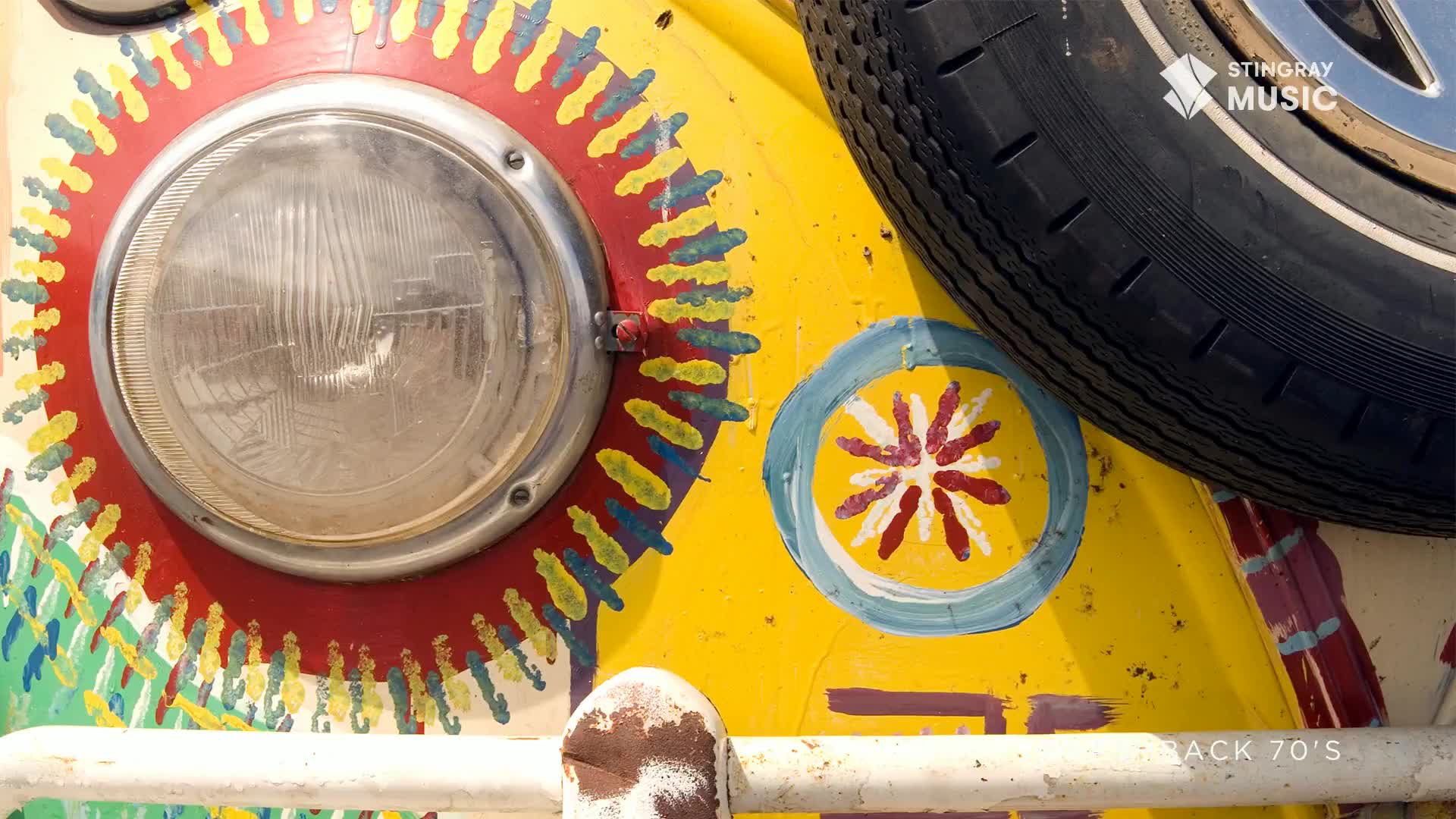 A bright yellow Volkswagen bus, painted with vibrant, psychedelic patterns, sits parked. Its spare tire is mounted on the front, a classic touch reminiscent of 70s Canadian road trips.