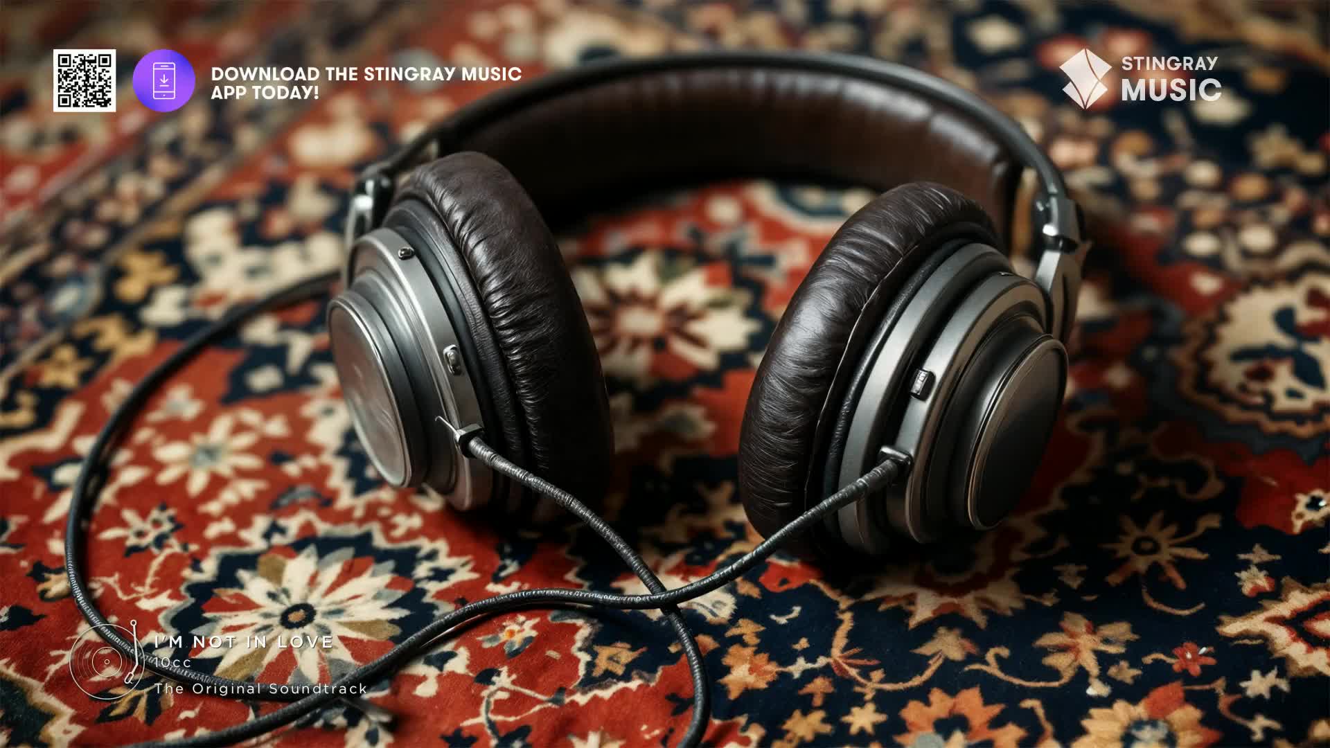 The worn leather of these headphones rests on a vibrant, patterned rug, reminiscent of a 70s Canadian living room. A black cord snakes across the fabric, connecting to the earcups.
