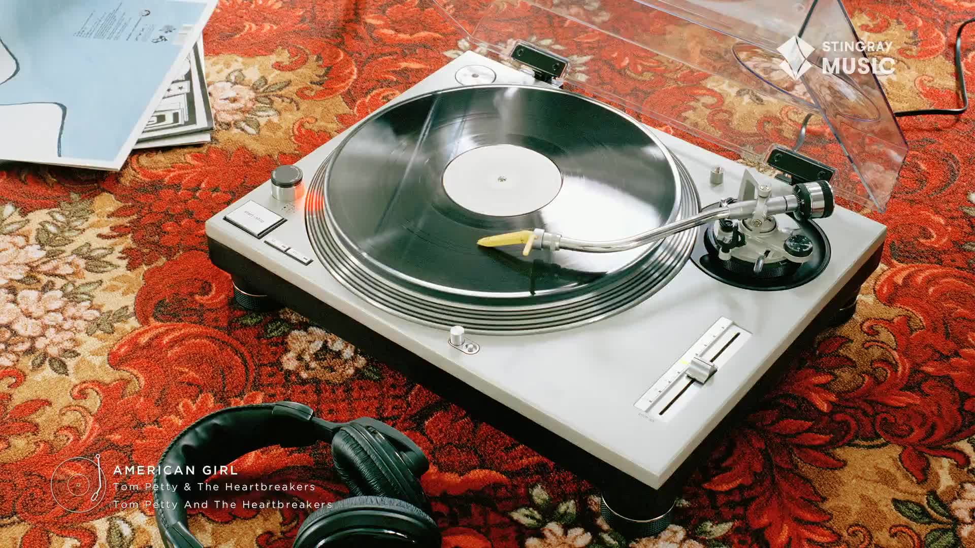 The needle drops onto the spinning vinyl, ready to play "American Girl." A pair of black headphones rests nearby on the patterned rug, waiting for the iconic 70s sound.