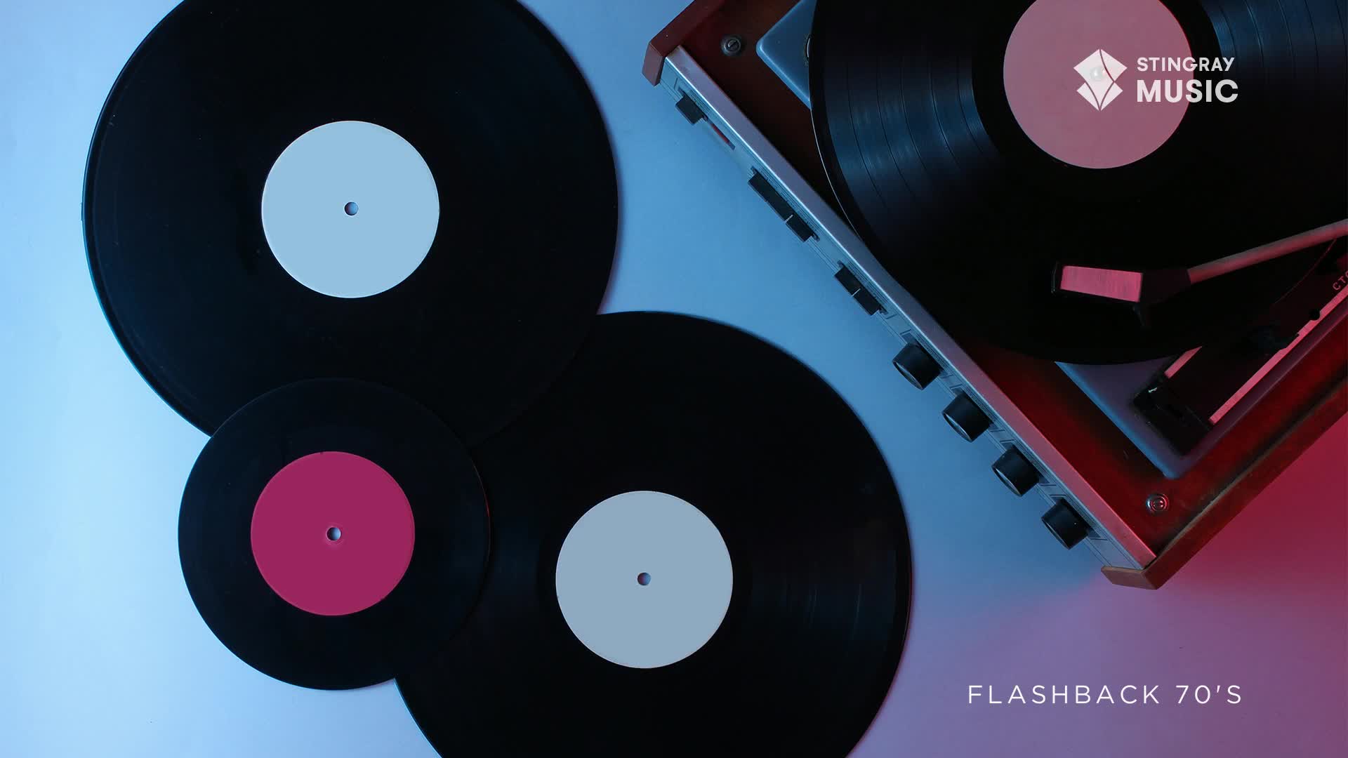 A turntable is spinning a record, its needle poised above the vinyl. Several other records, one with a bright pink label, are scattered around it.