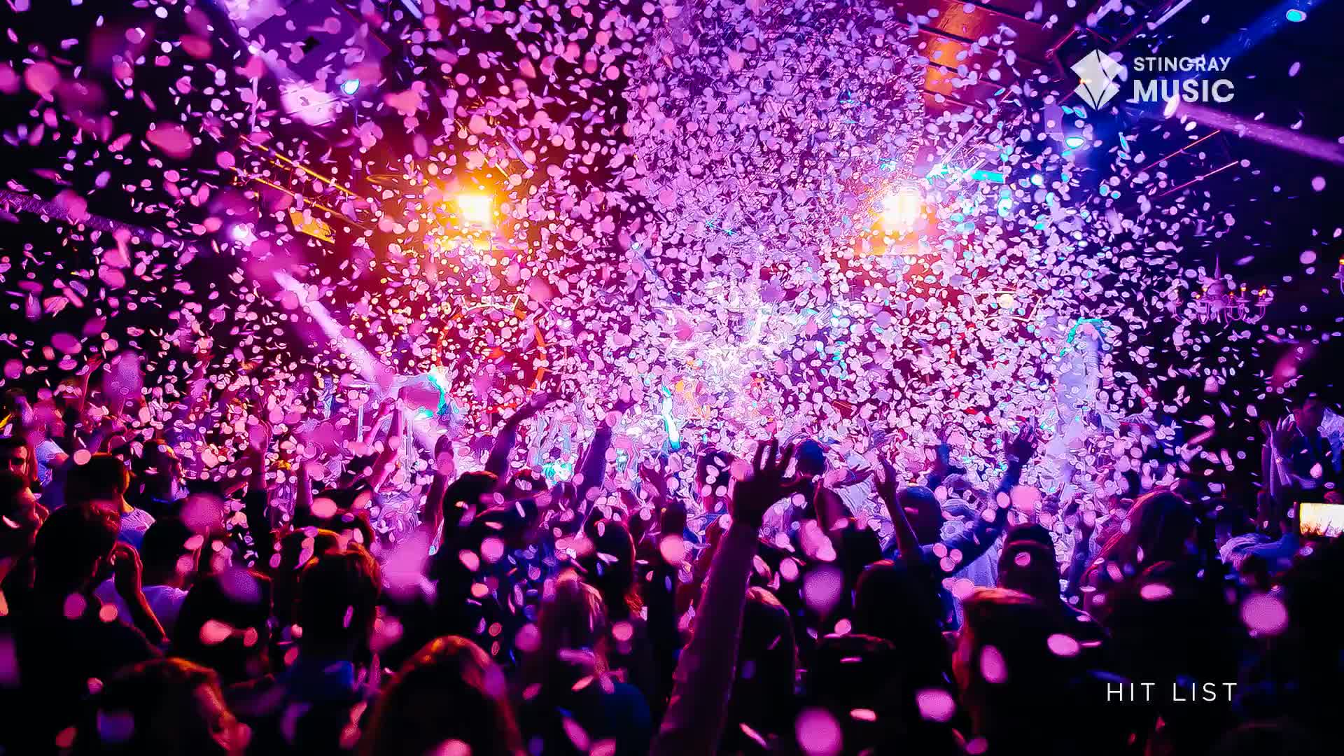 Confetti rains down on a crowd of people, their arms reaching up into the air.  The Stingray Hit List party is in full swing, bathed in purple and pink light.
