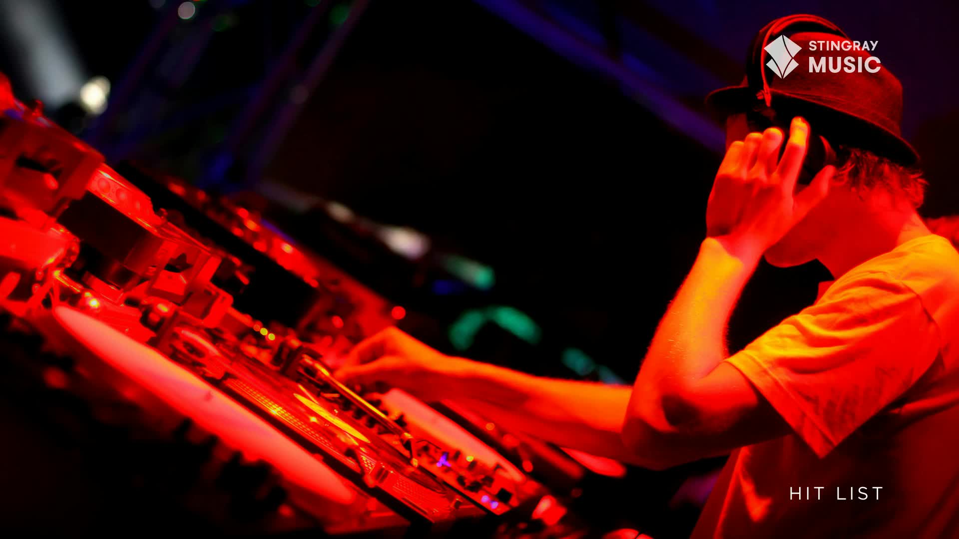 The DJ, bathed in red light, adjusts his headphones while his fingers dance across the turntables. The Stingray Hit List logo is visible, and the music is pumping.
