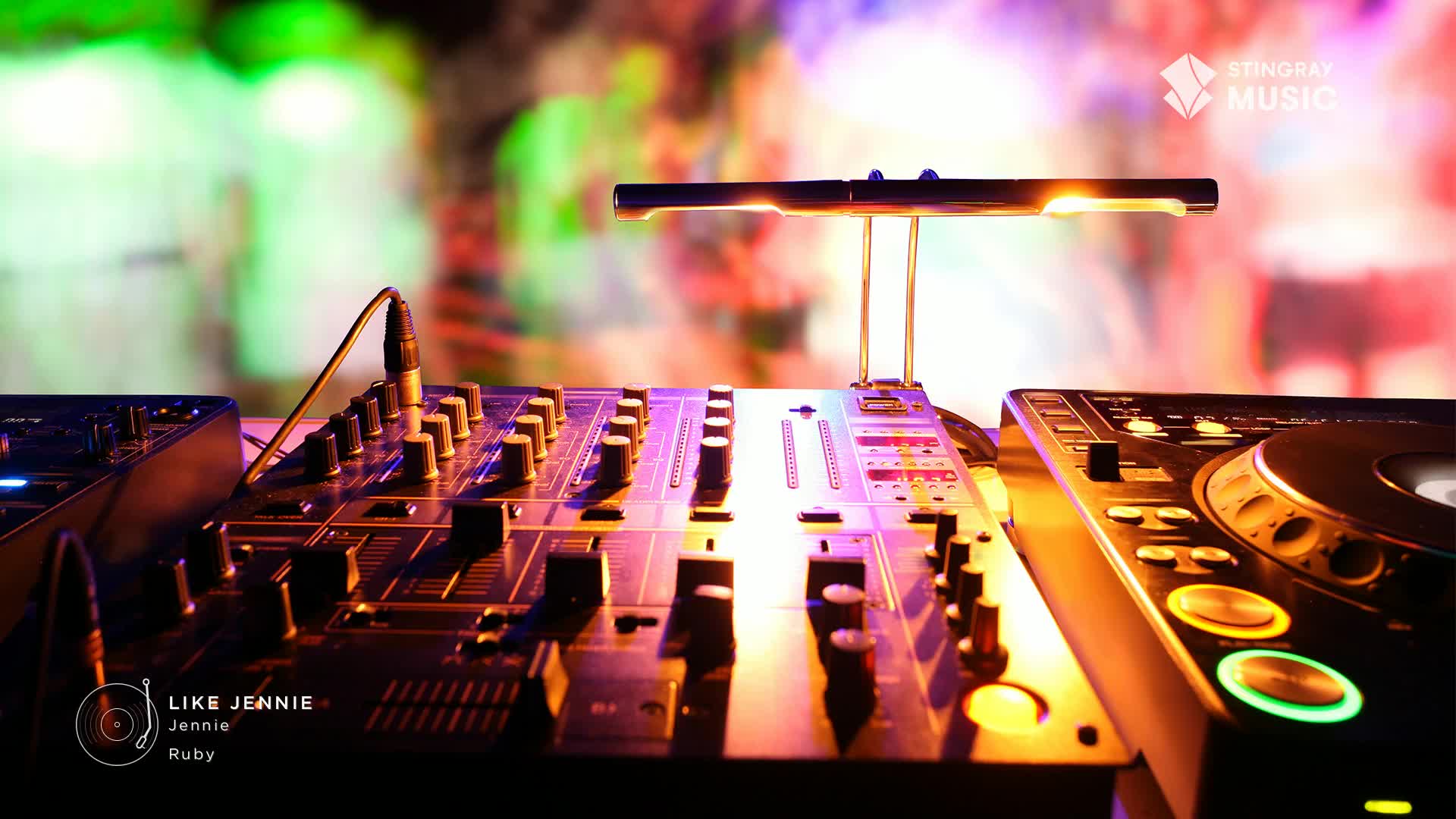 The DJ's mixer is lit up, ready for the next track on the Stingray Hit List. Behind the equipment, a crowd dances under colorful lights, the energy palpable.
