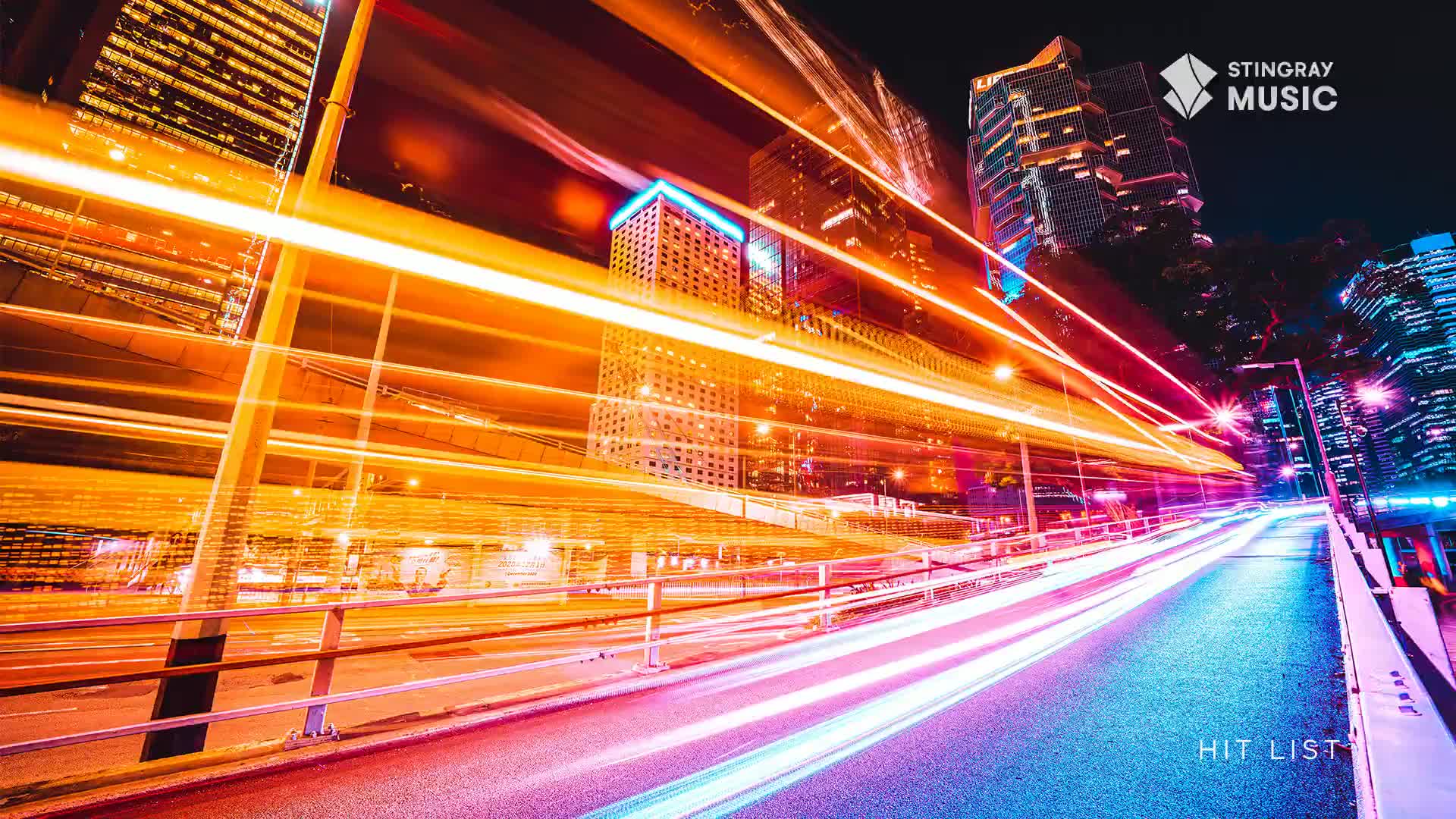 Streaks of orange and white light race down the road, a stark contrast to the city's glowing buildings. The "Hit List" logo, a nod to Stingray Music, is visible on the road's edge.

