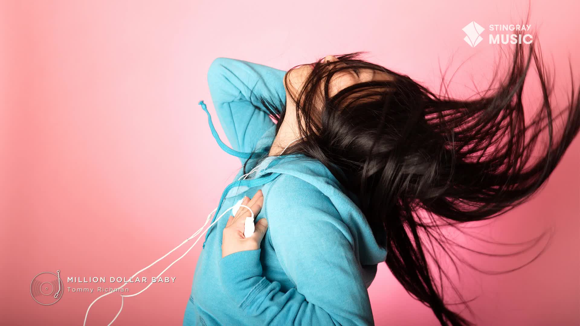 A woman in a blue hoodie throws her head back, dark hair streaming across a pink background. She's listening to "Million Dollar Baby" on the Stingray Hit List, the white earbuds dangling from her hand.
