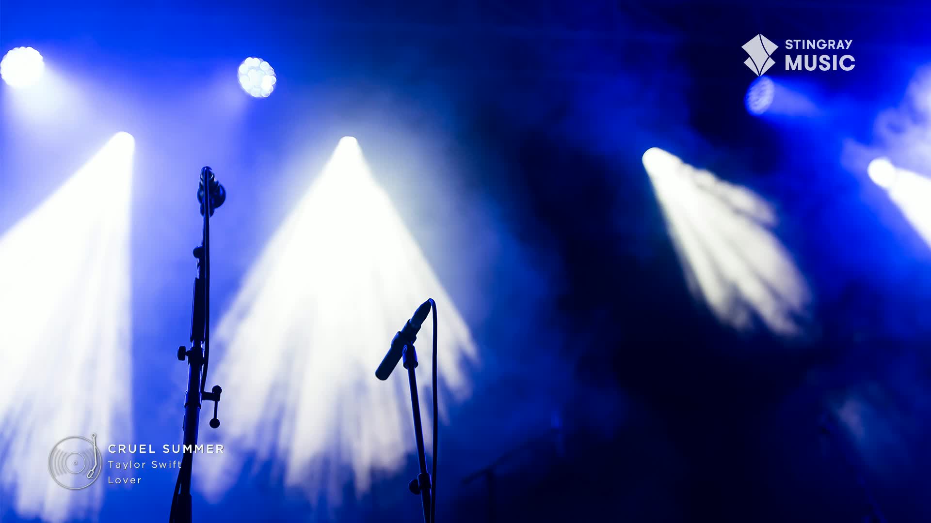Microphone stands stand silhouetted against the bright stage lights, ready for Taylor Swift on the Stingray Hit List. The blue and white beams cut through the air, illuminating the Cruel Summer performance.
