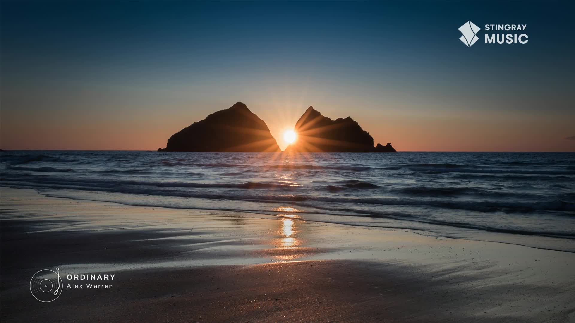 The sun is setting between two dark, rocky islands, casting a golden glow on the water. The waves gently lap the shore, reflecting the sky's warm colours as "Ordinary" by Alex Warren plays on the Stingray Hit List.
