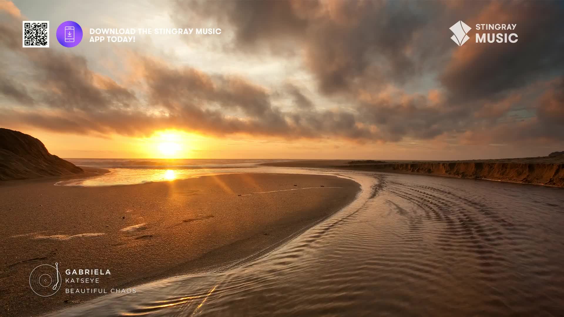 The sun is setting, casting a warm glow over the beach and water. A river carves its way through the sand, its surface rippled by a gentle breeze.
