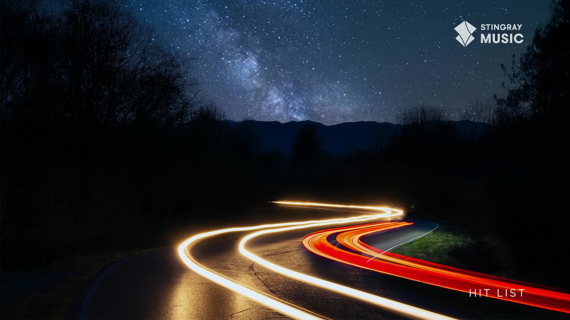 Headlights streak along the winding road, leaving trails of light under the Canadian night sky. The Stingray Hit List logo sits in the corner, a reminder of the music that fuels the journey.

