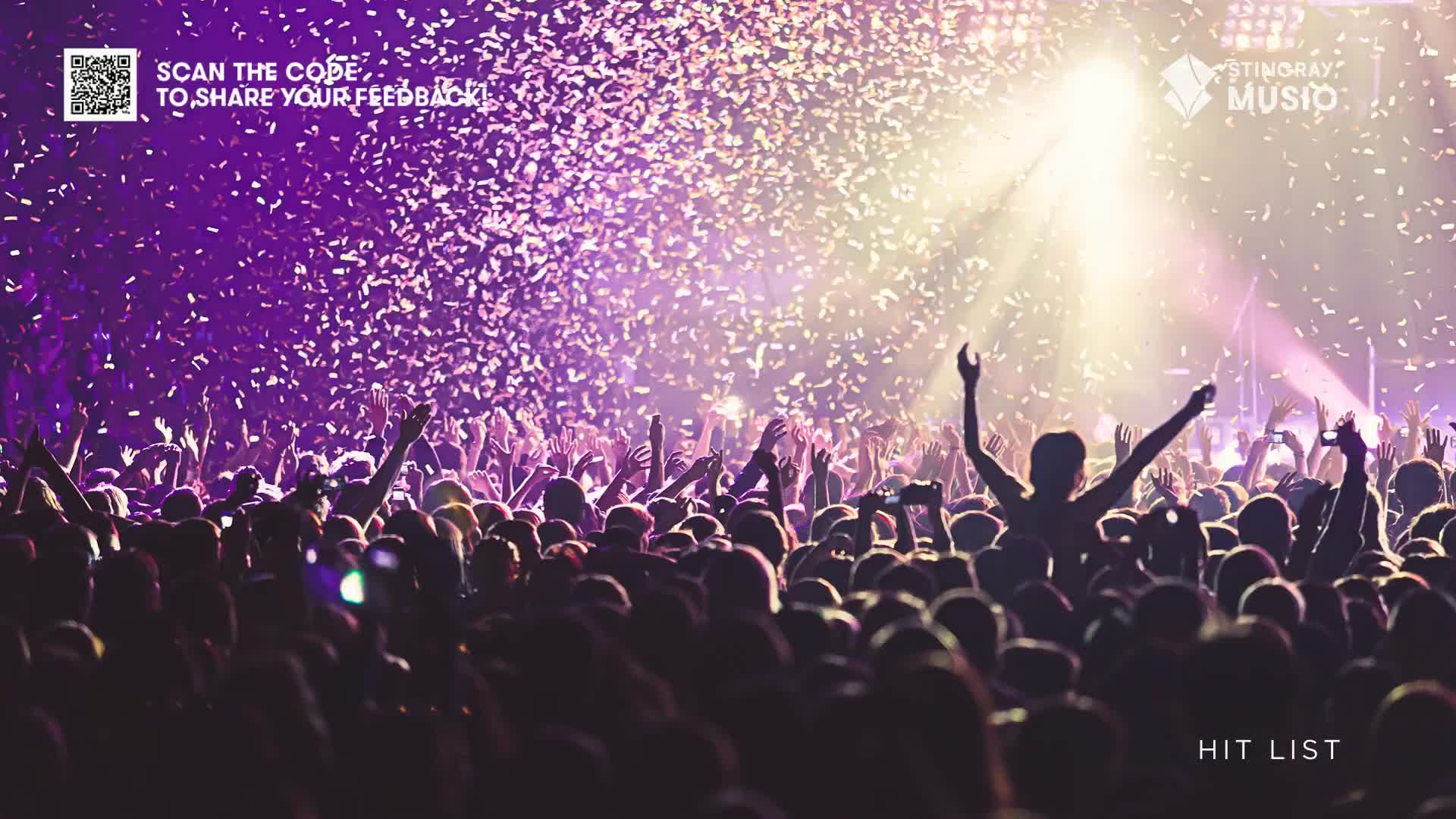 Confetti rains down on a packed crowd, illuminated by a bright spotlight. Arms are raised as people cheer, likely enjoying a live music event in Canada, possibly a Stingray Hit List show.
