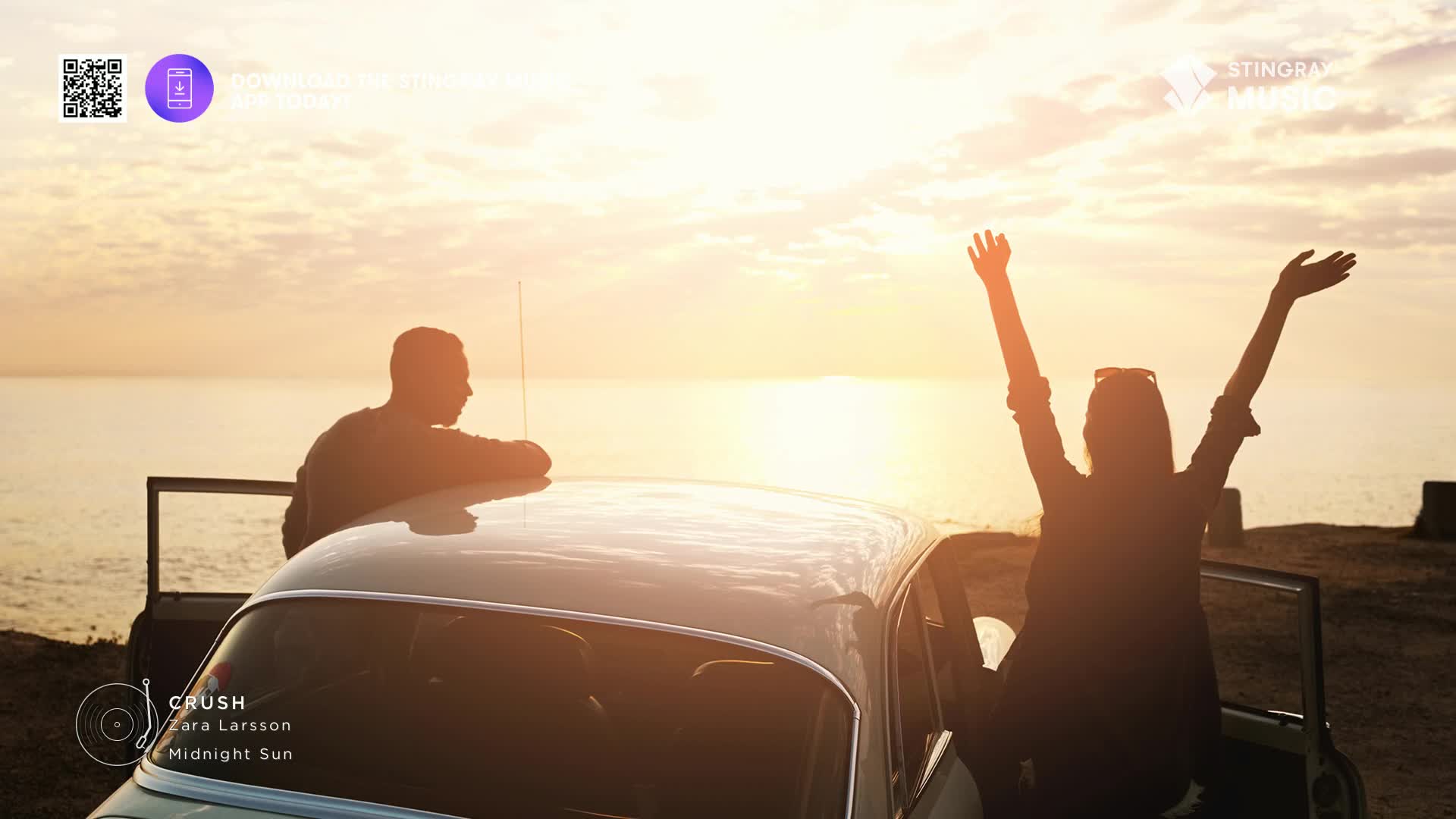 The sun is setting over the water, and a woman is sitting in a car with her arms raised. Beside her, a man leans on the car's roof, silhouetted against the bright sky.
