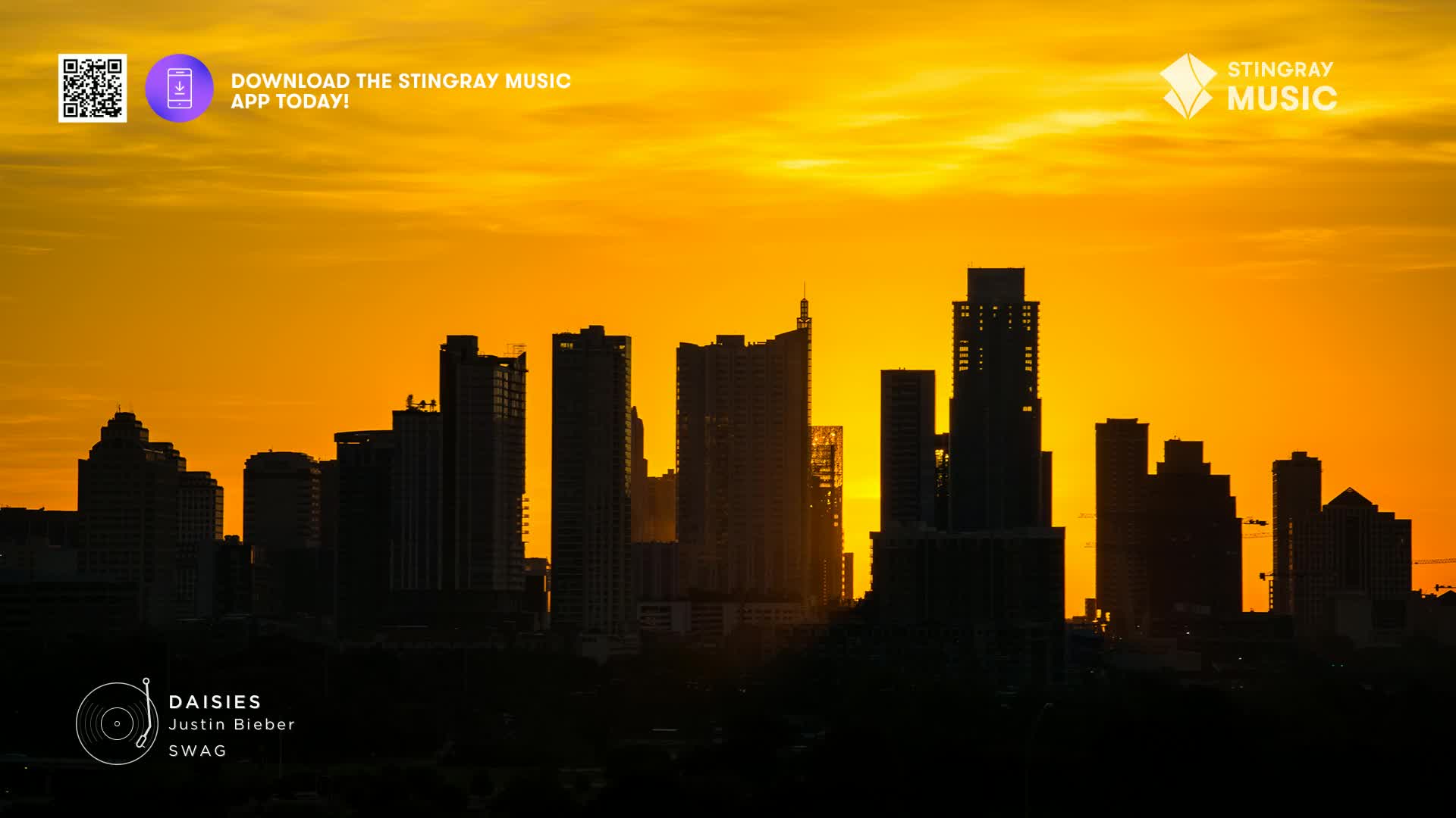 The sun bleeds orange behind the city skyline, silhouetting the buildings. The Stingray Music logo and a QR code are visible in the top corners, and the song "Daisies" by Justin Bieber is playing.
