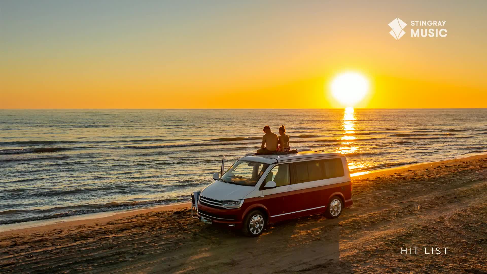 A couple sits atop a maroon and white van parked on the beach, watching the sun dip below the horizon. The Stingray Hit List logo floats in the corner, a reminder of the music playing as the waves gently lap the shore.
A couple sits atop a maroon and white van parked on the beach, watching the sun dip below the horizon. The Stingray Hit List logo floats in the corner, a reminder of the music playing as the waves gently lap the shore.