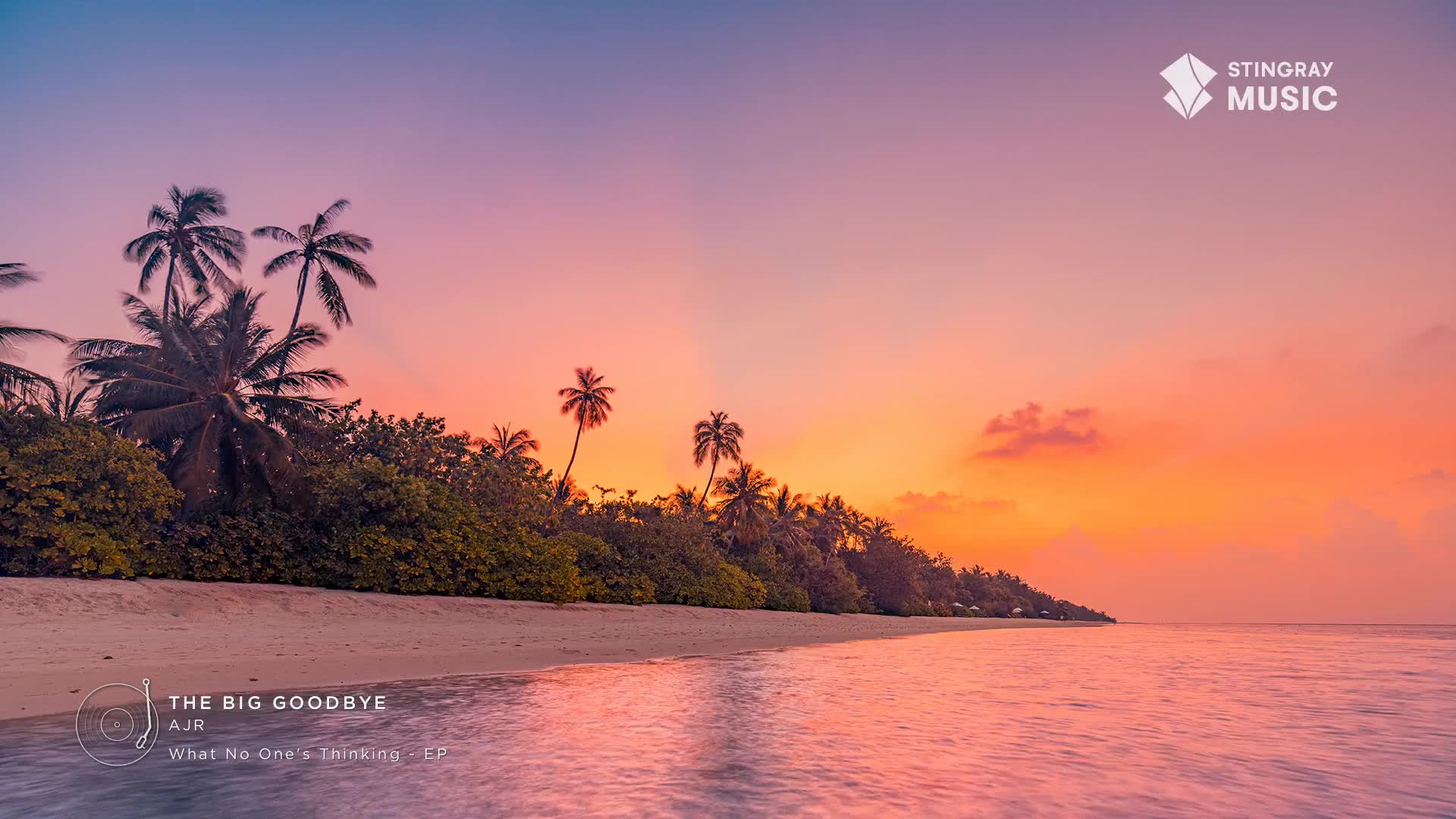 The ocean laps gently onto a sandy beach lined with palm trees. A vibrant sunset paints the sky in hues of orange and pink.
