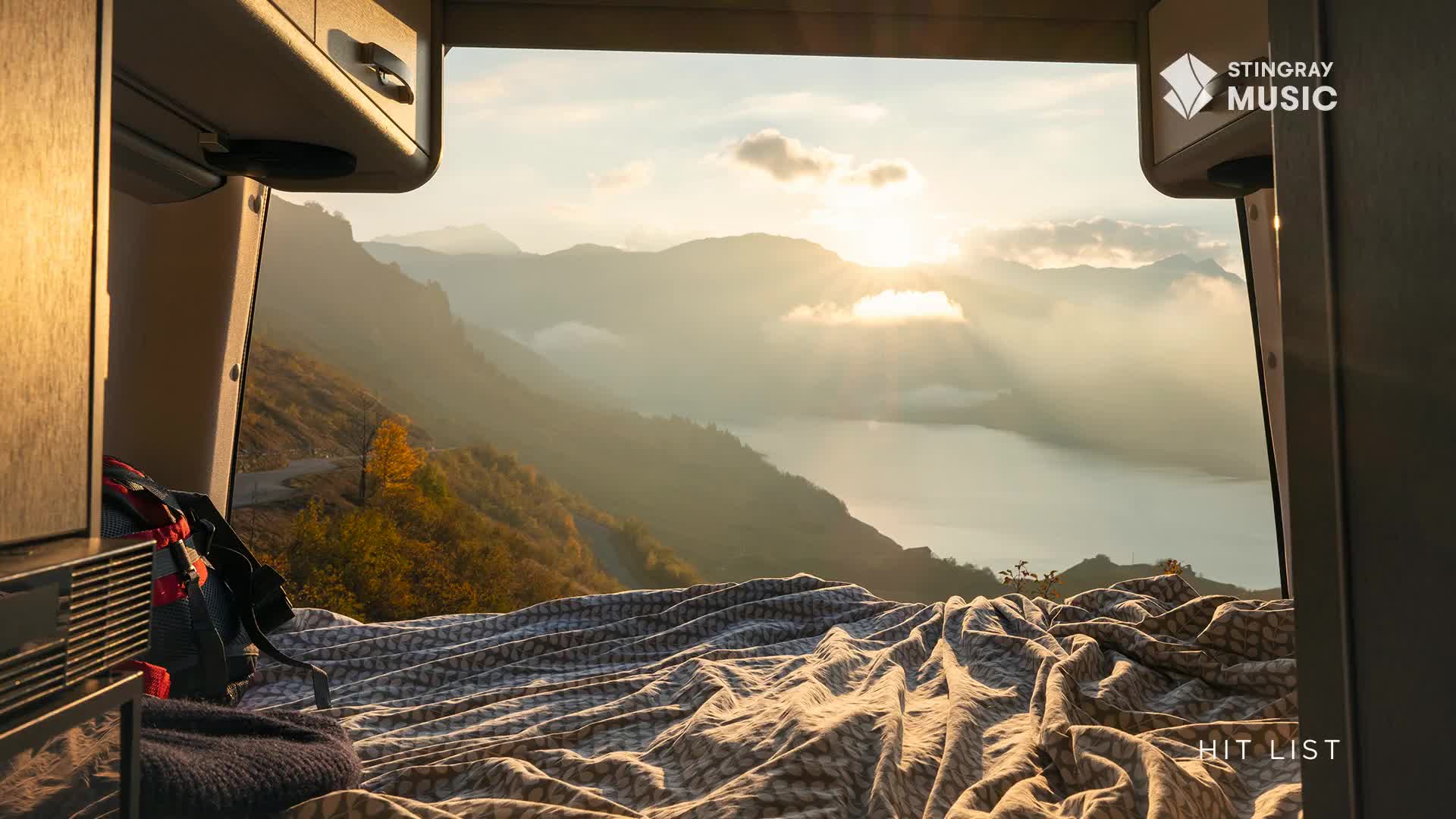 The sun breaks through the clouds, illuminating a vast Canadian landscape of mountains and a lake. A rumpled blanket covers a bed, hinting at a recent rest stop on this Stingray Hit List journey.