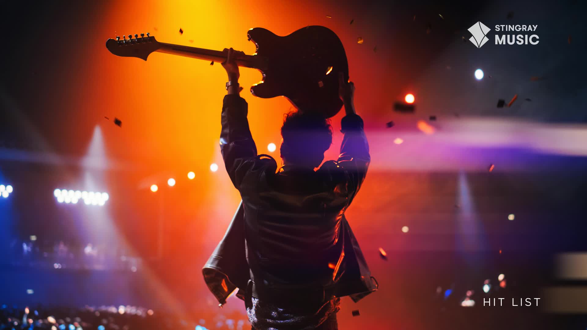Confetti rains down as a performer raises a guitar above their head on a stage bathed in orange and blue light. The Stingray Music logo appears in the upper right corner, with "HIT LIST" at the bottom.