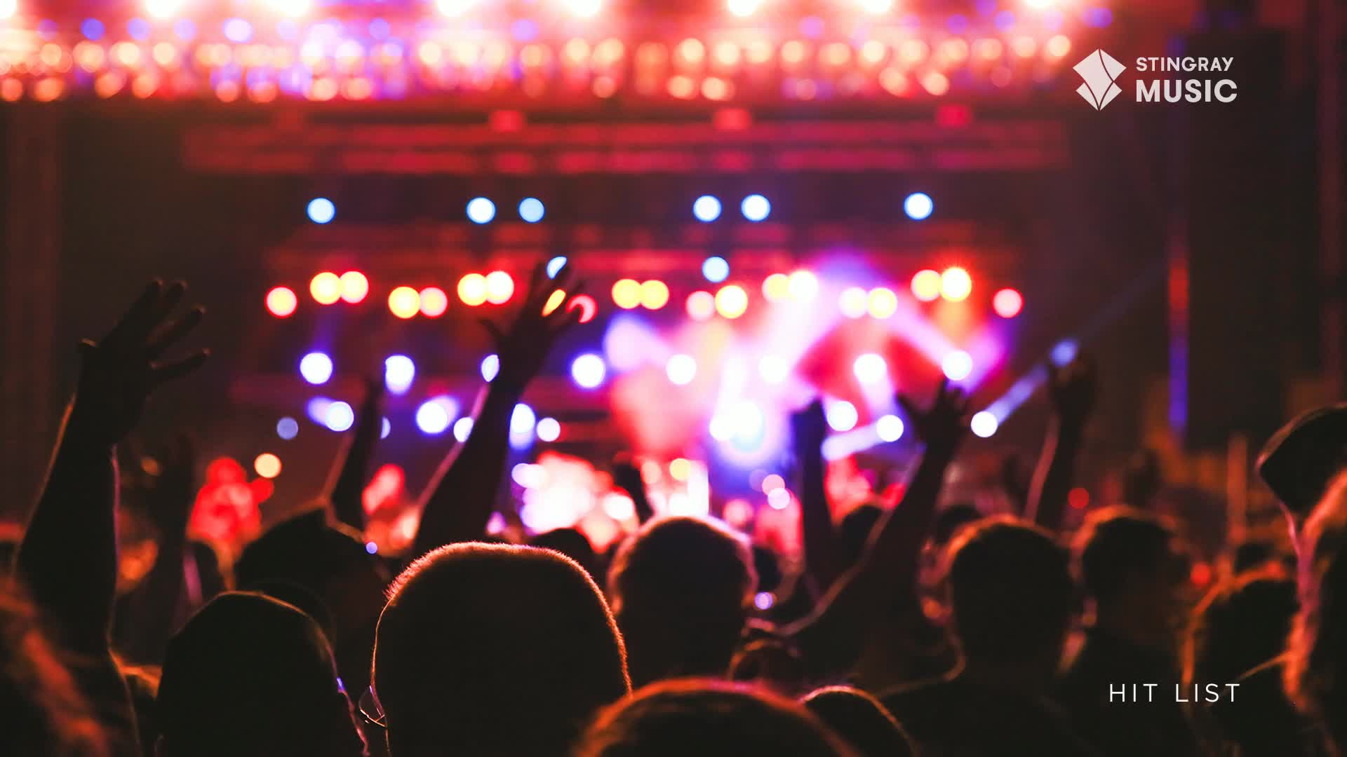Hands are raised in the air, silhouetted against a stage bathed in red and purple lights. The crowd is packed tight, a sea of heads and arms reaching towards the performers.