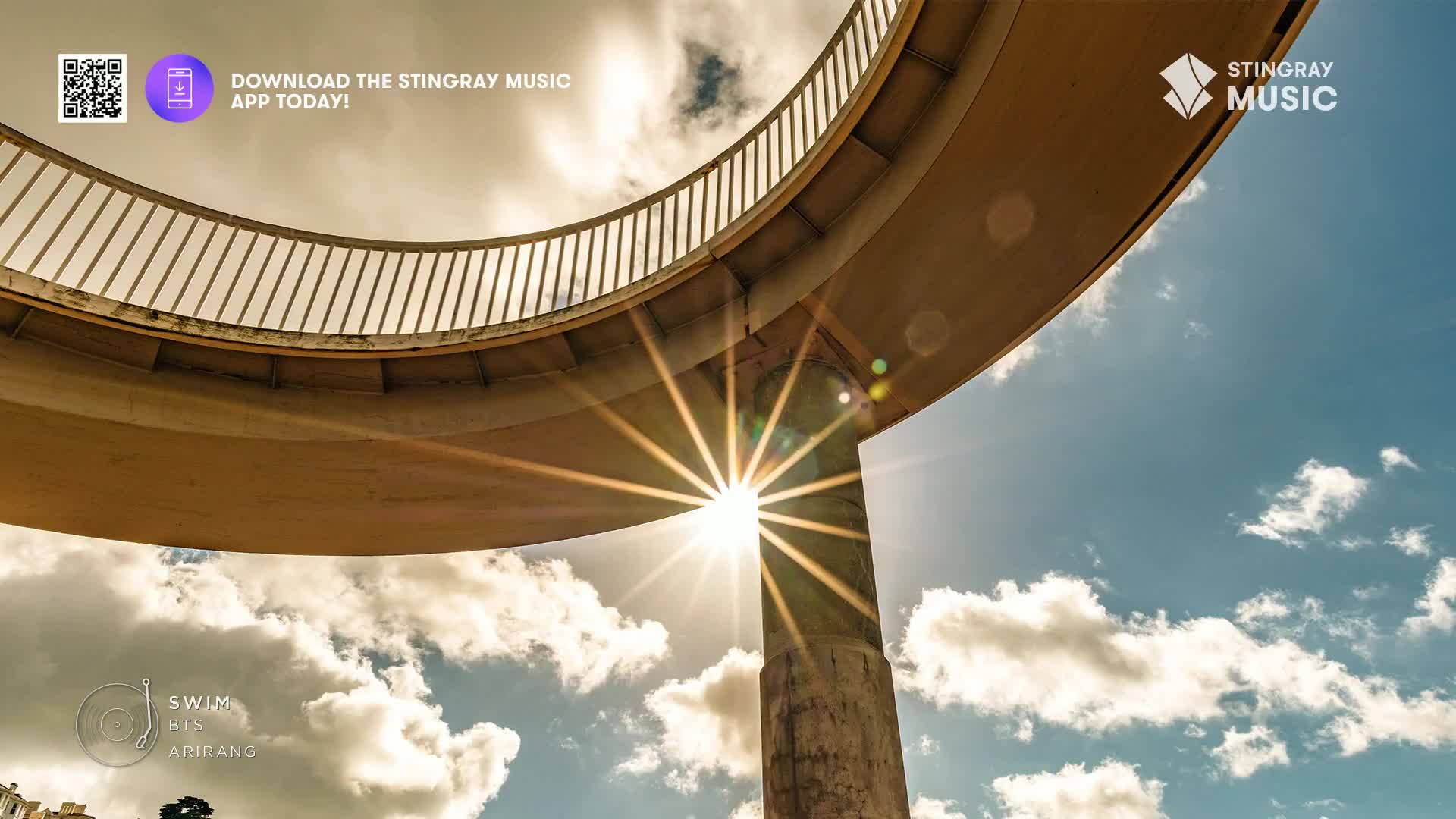 The sun bursts through the concrete support of an overpass, its rays fanning out across a bright blue sky dotted with clouds. This Canadian scene, perhaps a backdrop for a Stingray Hit List feature, feels vast and open.